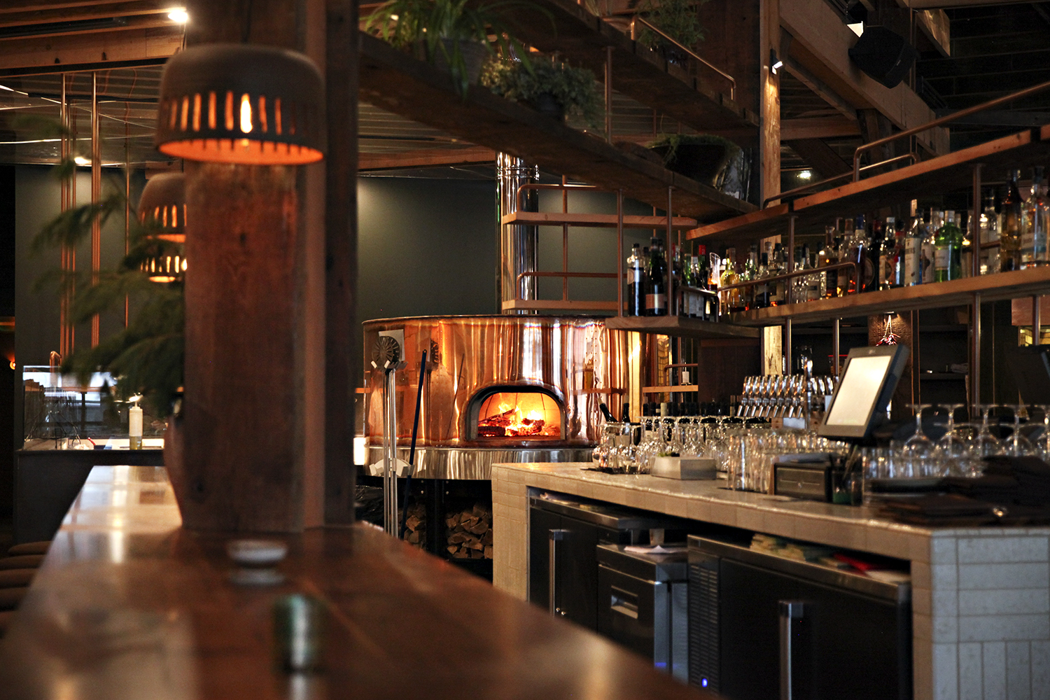 A large copper pizza oven in the background, and a wooden bar in the foreground.