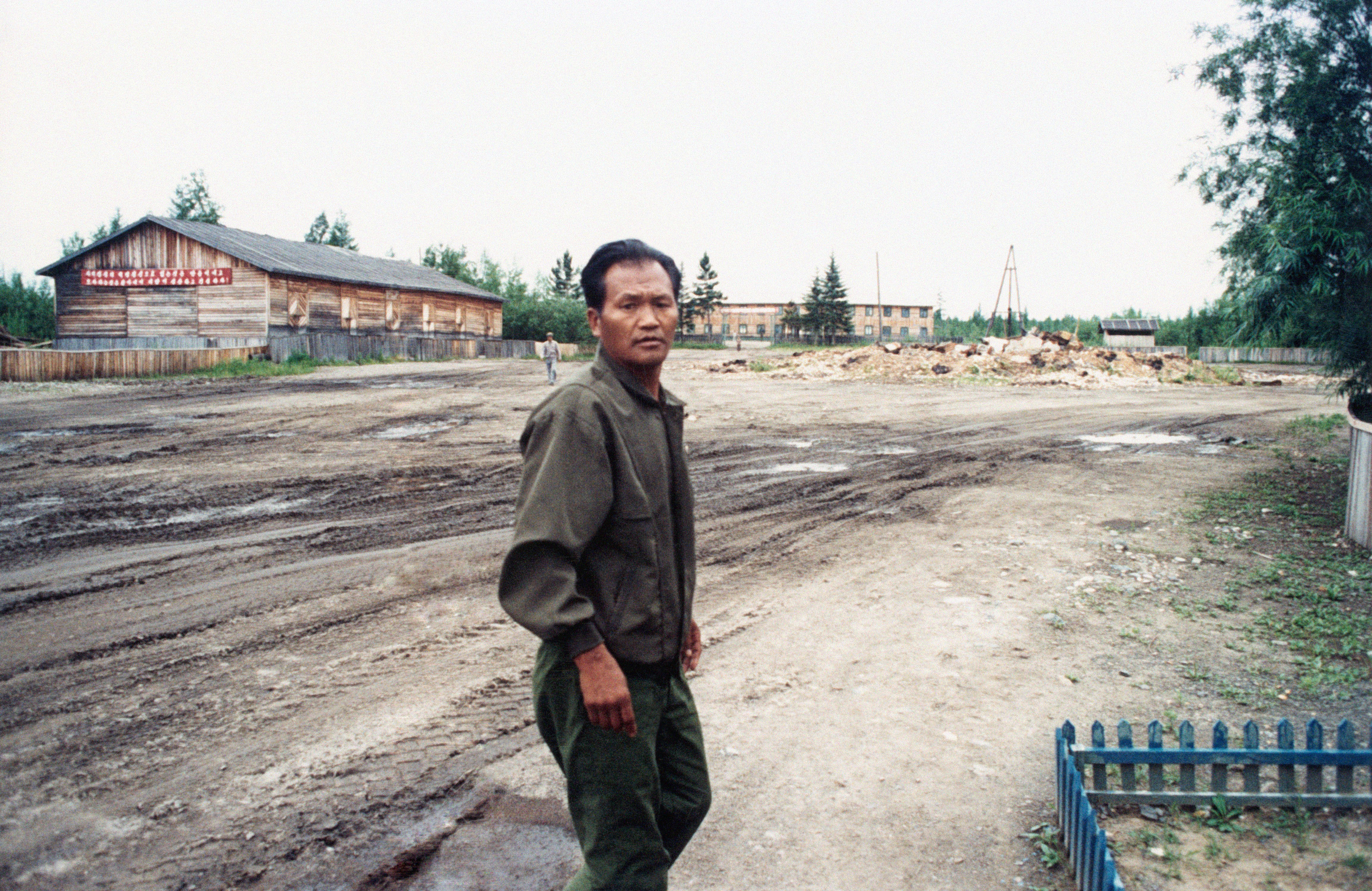 A man stands in front of barracks and bare dirt at North Korea’s gulag in Siberia, Khabarovsk Territory, Chegdomynsky District, Zimovye, 2001.
