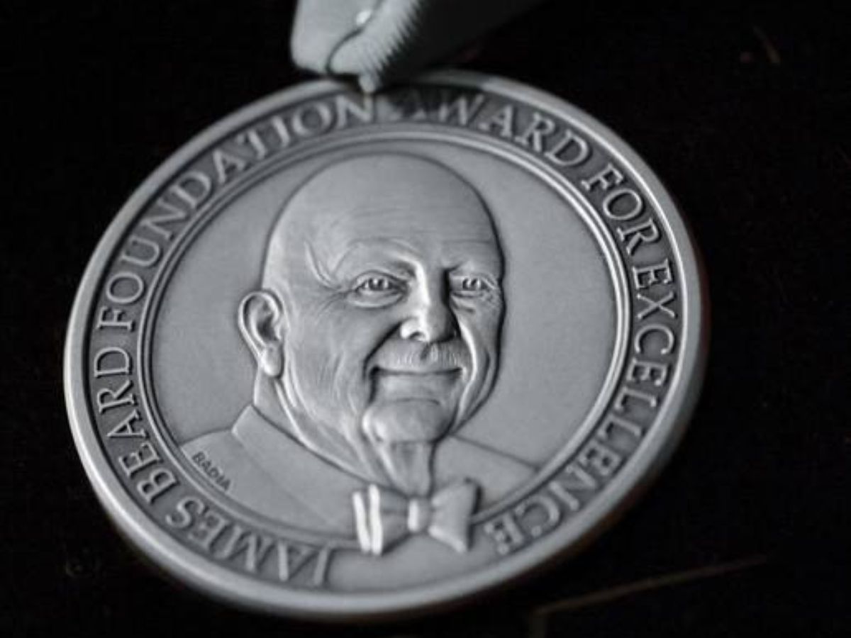 A silver James Beard medal is isolated on a black background