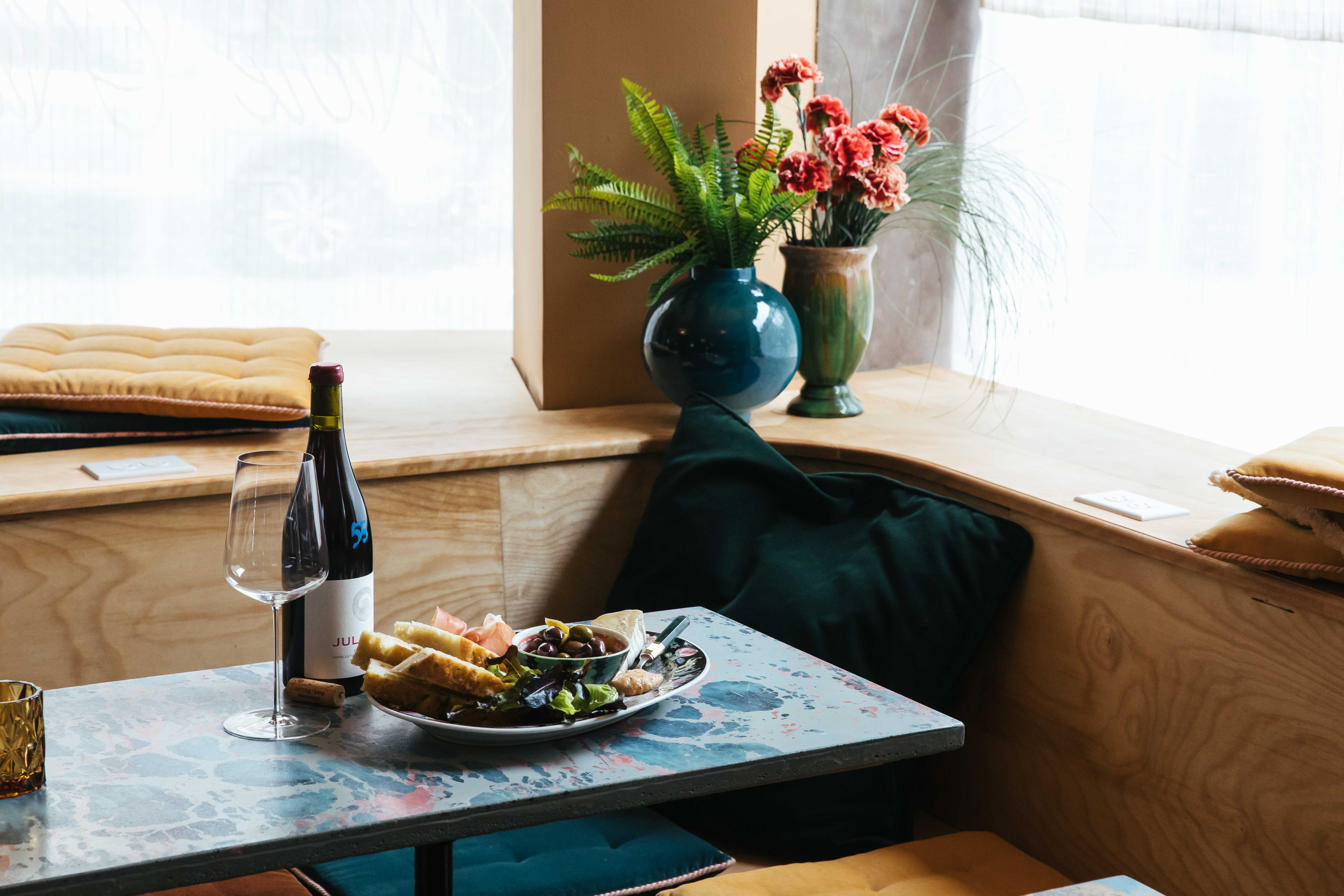 A plate of food and a bottle of wine sit on a blue table at Niche Niche.
