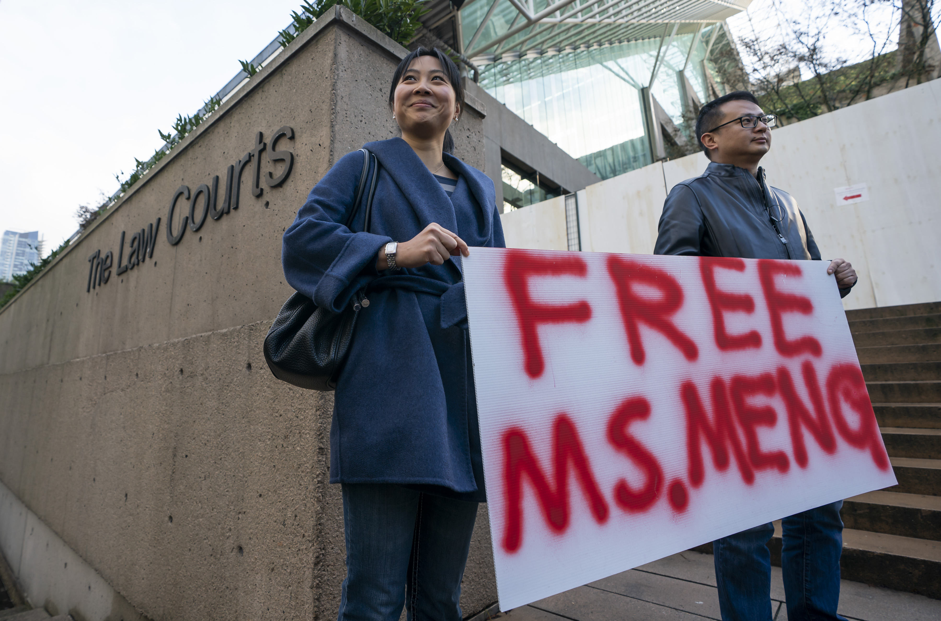 Two people stand outside a Vancouver courthouse holding a sign reading “Free Ms. Meng.”