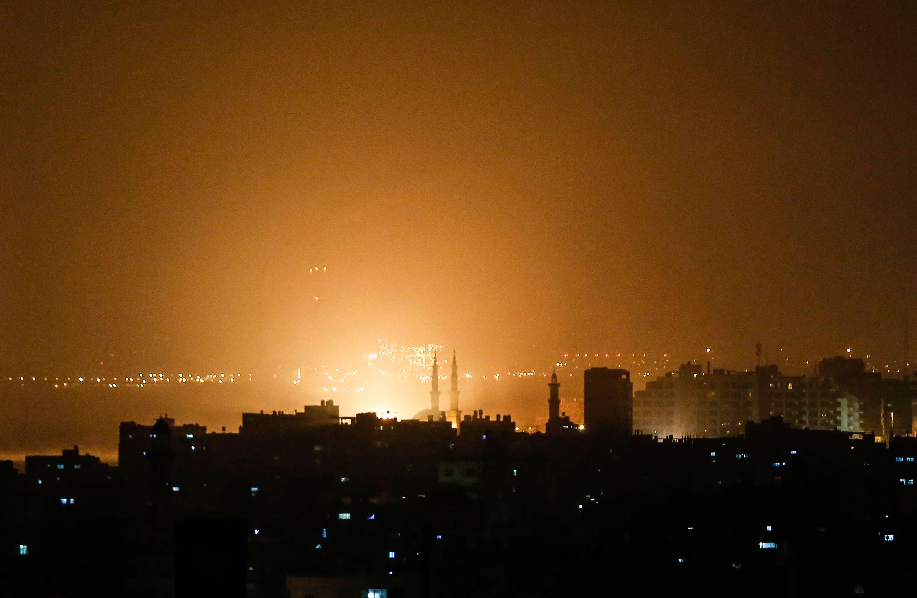 The sky above buildings on the Gaza Strip glows orange during an Israeli air strike in Gaza city late on March 14, 2019.