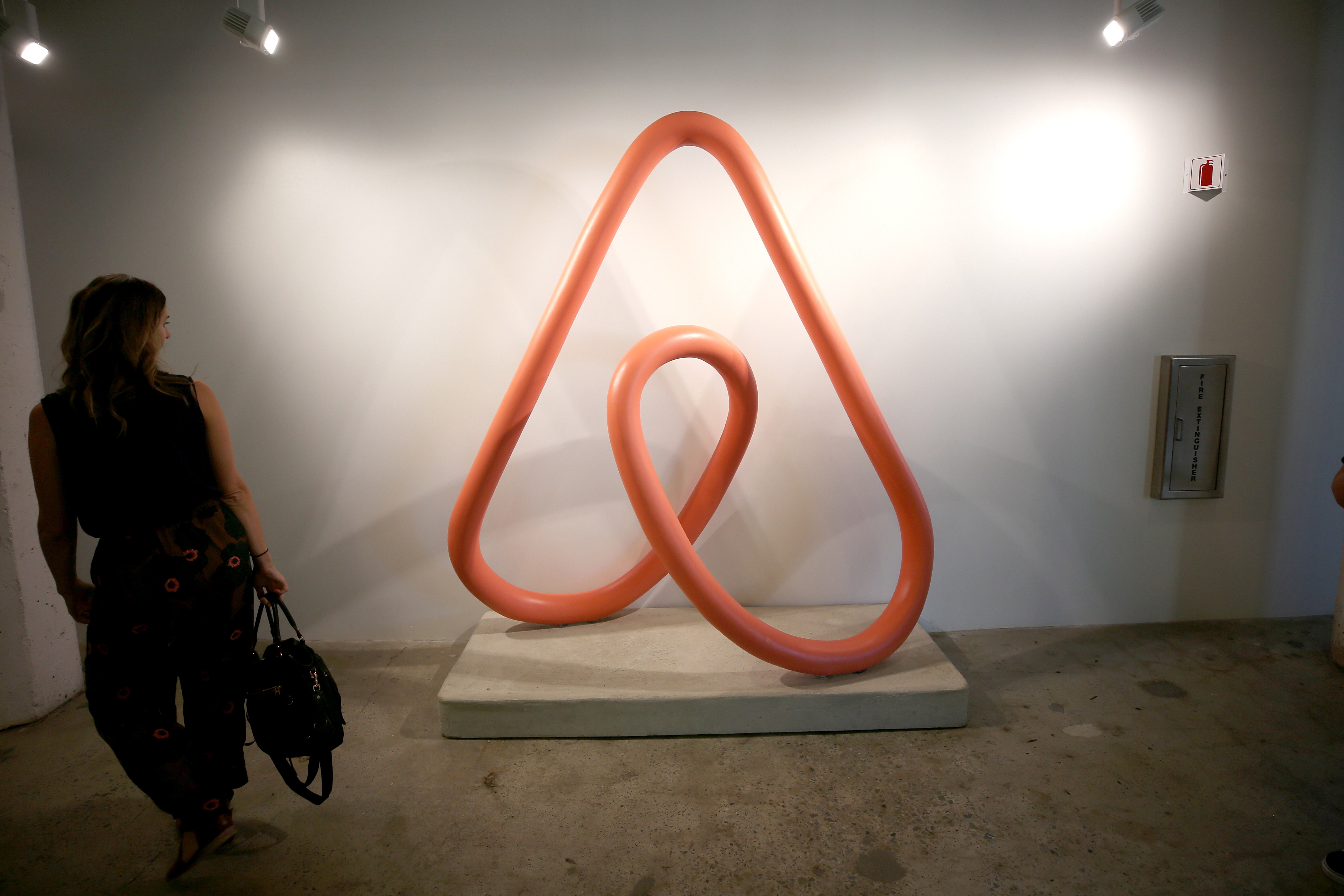 A woman stands looking at a sculpture of the Airbnb logo.