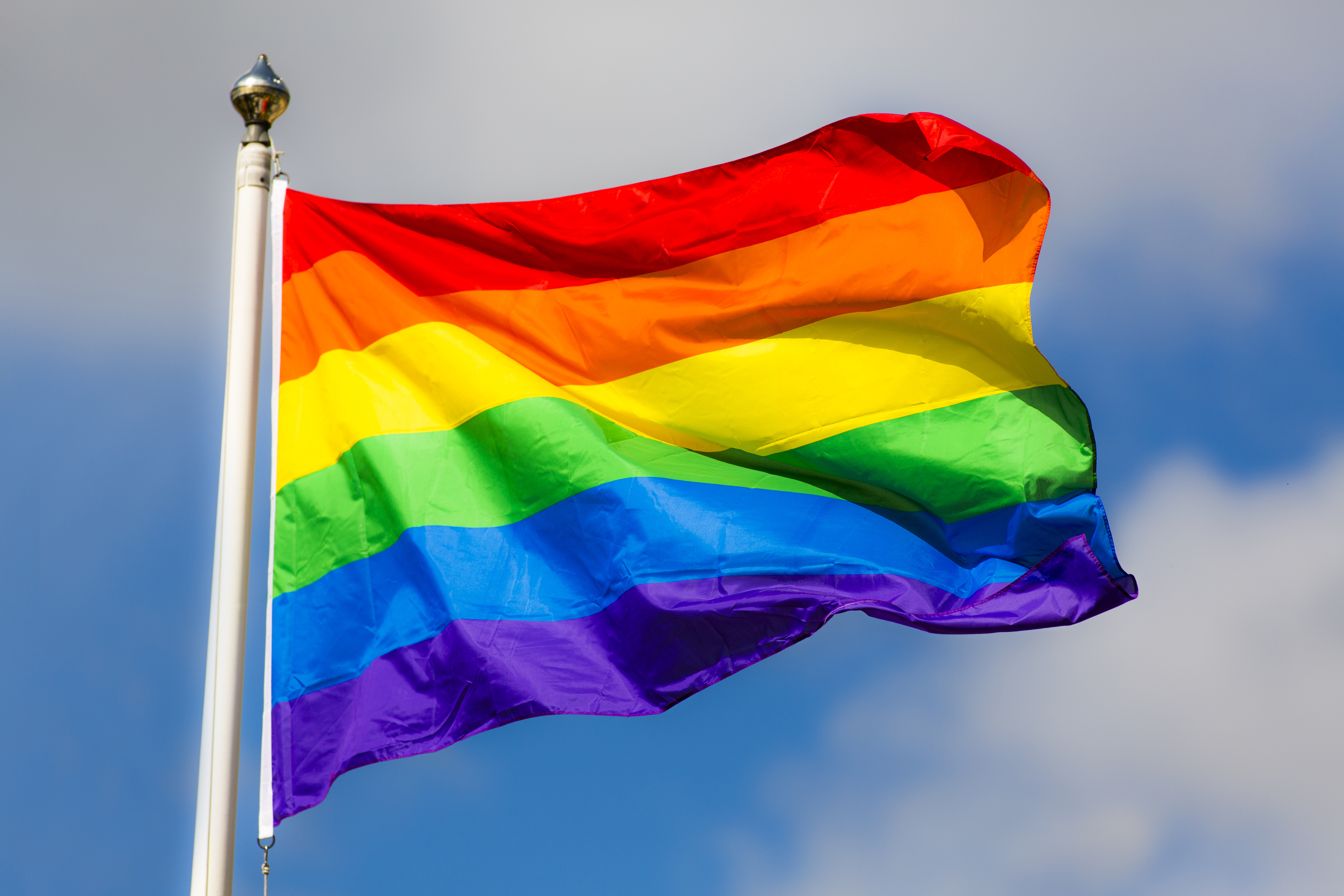 A rainbow flag in front of a blue sky.