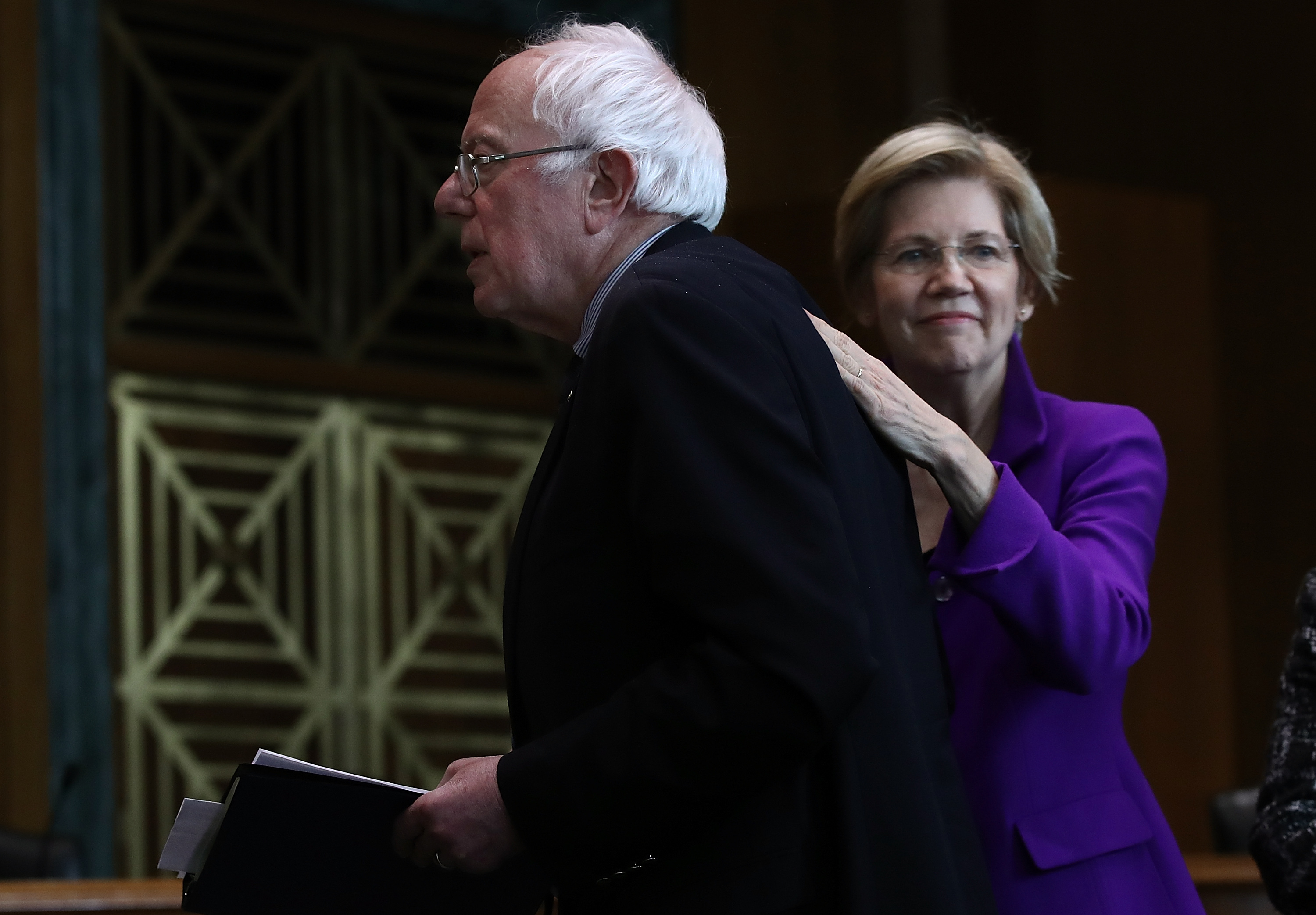 Sen. Elizabeth Warren (R) (D-MA) pats Sen. Bernie Sanders (L) (I-VT) on the back.
