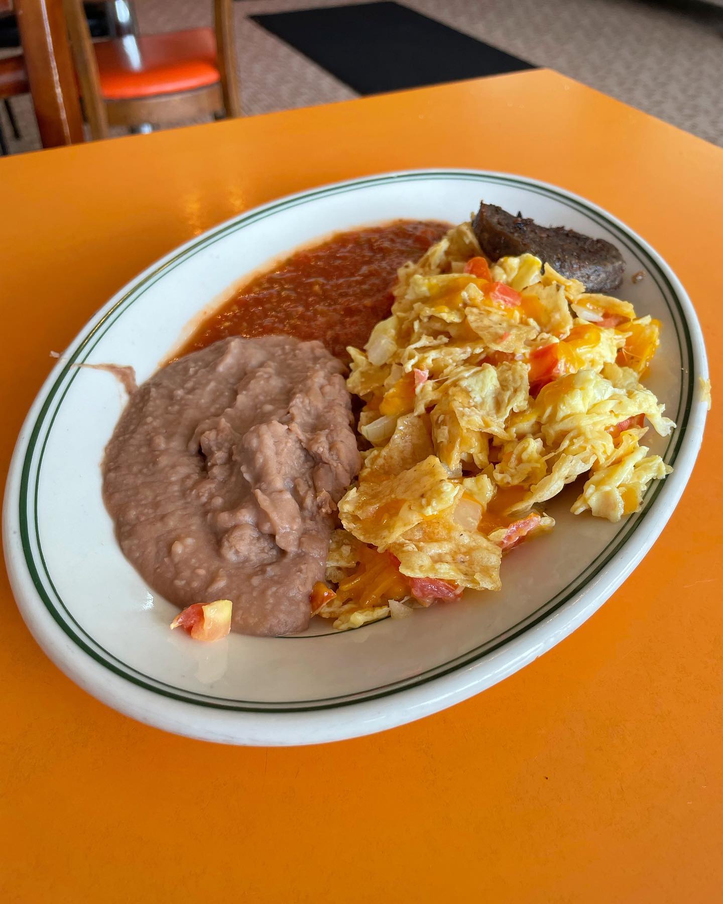 A plate of eggs with chips, refried beans, and red sauce.