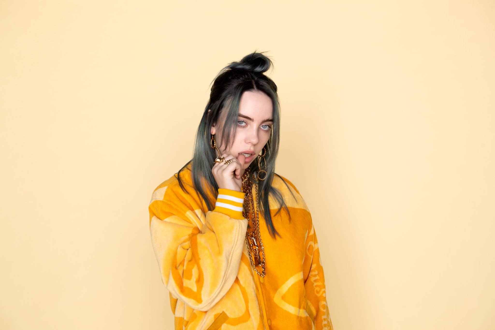 Billie Eilish stares at the camera against a yellow background.