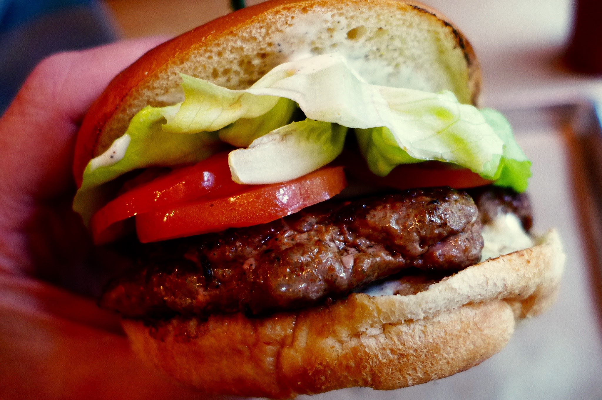 A close-up picture of a burger with tomato and iceberg lettuce.