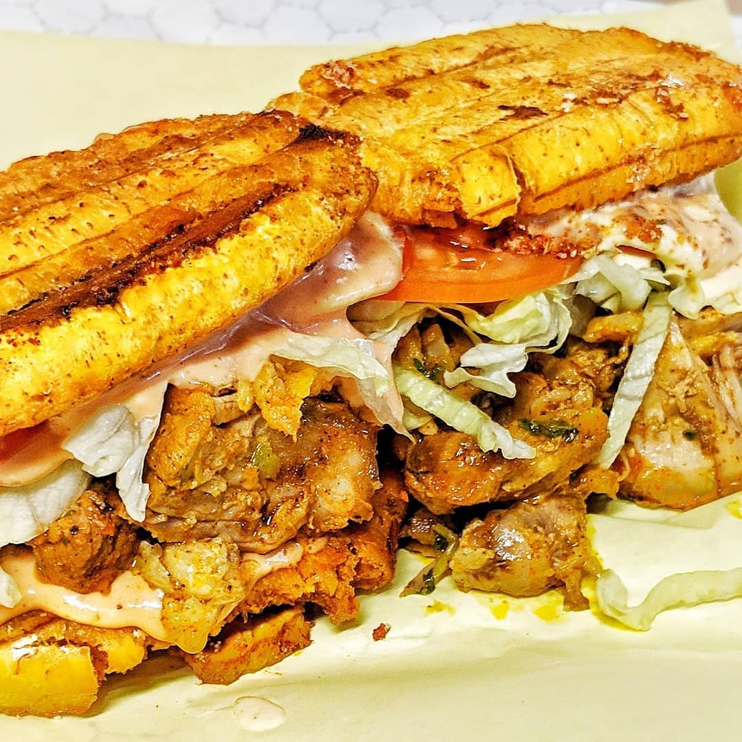 A closeup of a jibarito, filled with shredded pork and lettuce, served with fried plantains
