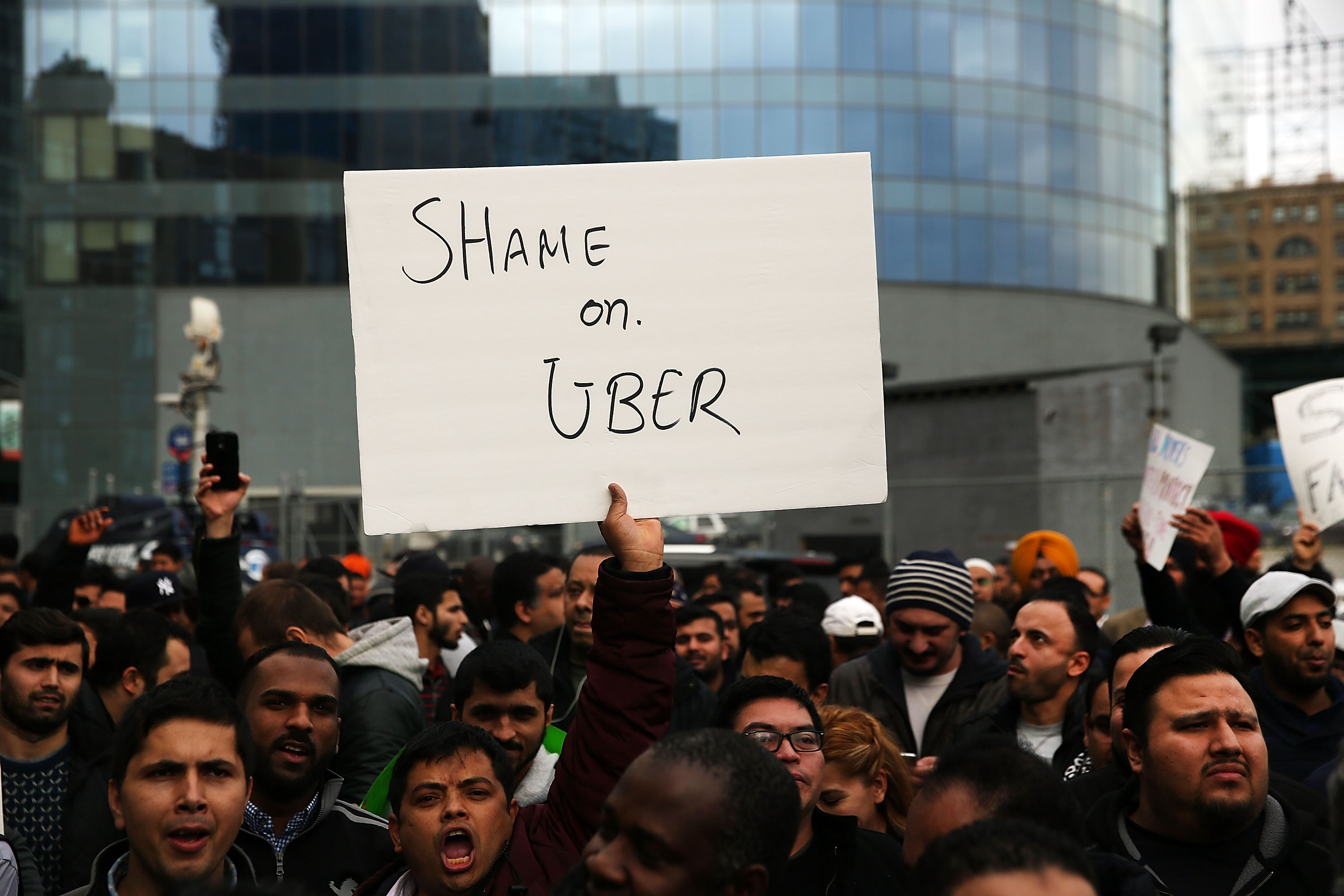 Crowd with person holding up sign that says “Shame on Uber”