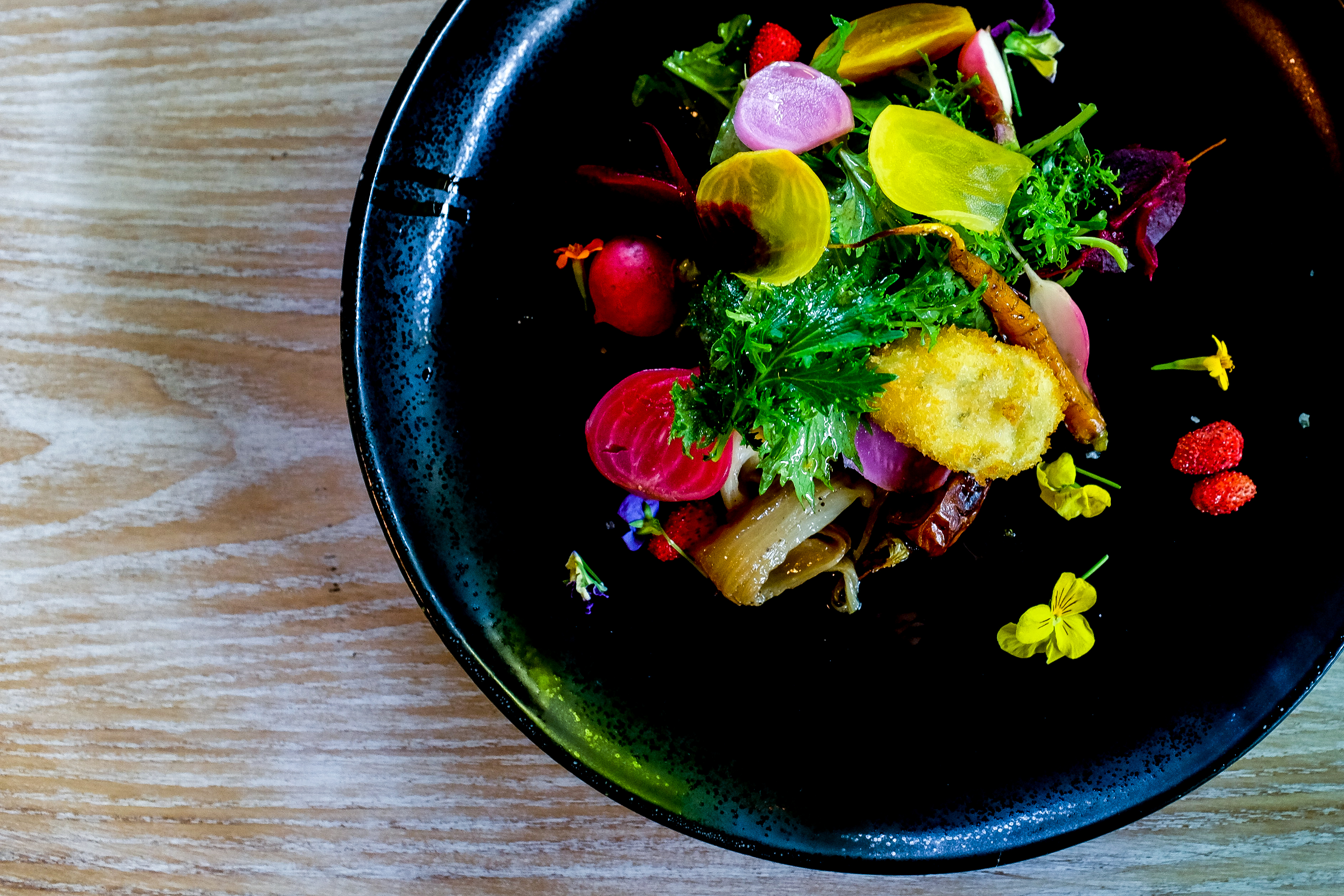a salad with yellow and pink radishes in a black bowl.