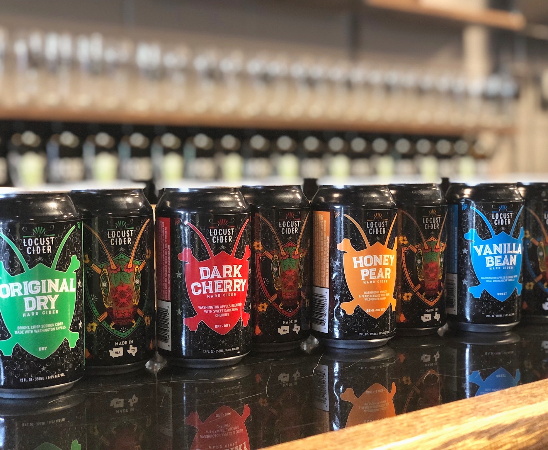 A line of Locust Cider cans sitting on a bar