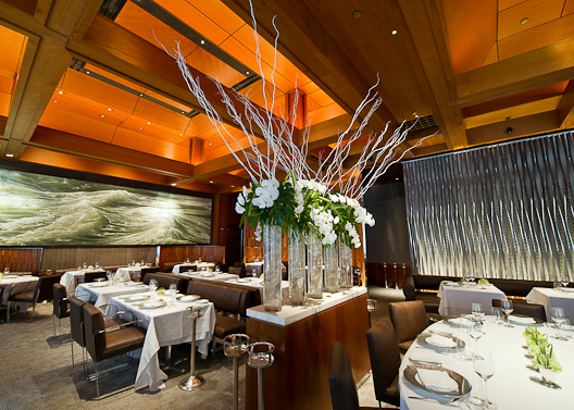 Le Bernardin’s dining room has a floral arrangement in the middle with white flowers, plus tables with white tablecloths