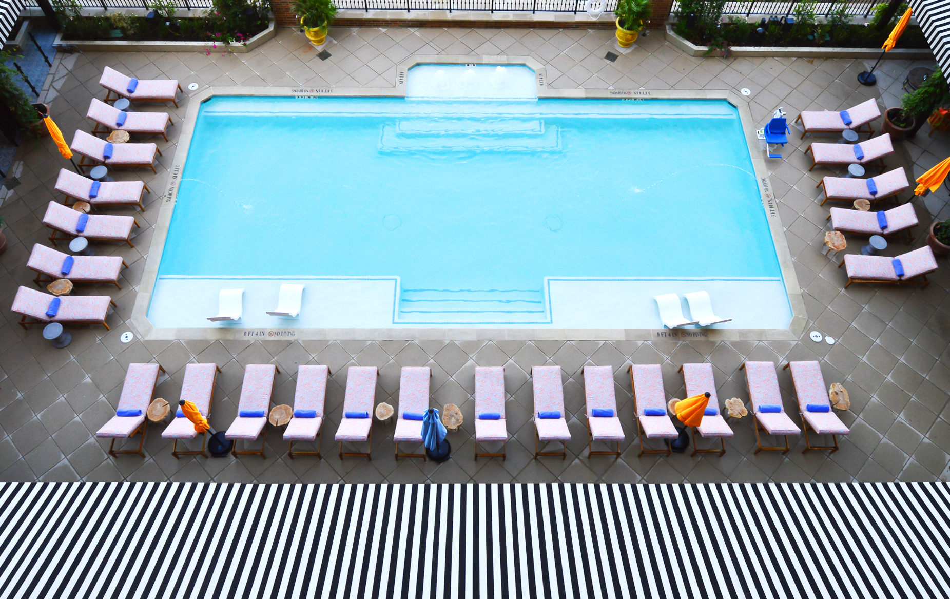 Blue pool with pink chairs and black and white awning