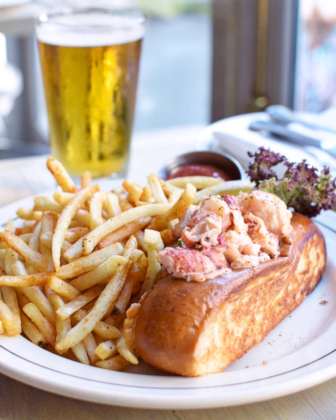A buttered roll overflowing with lobster appears on a plate beside a pile of french fries.