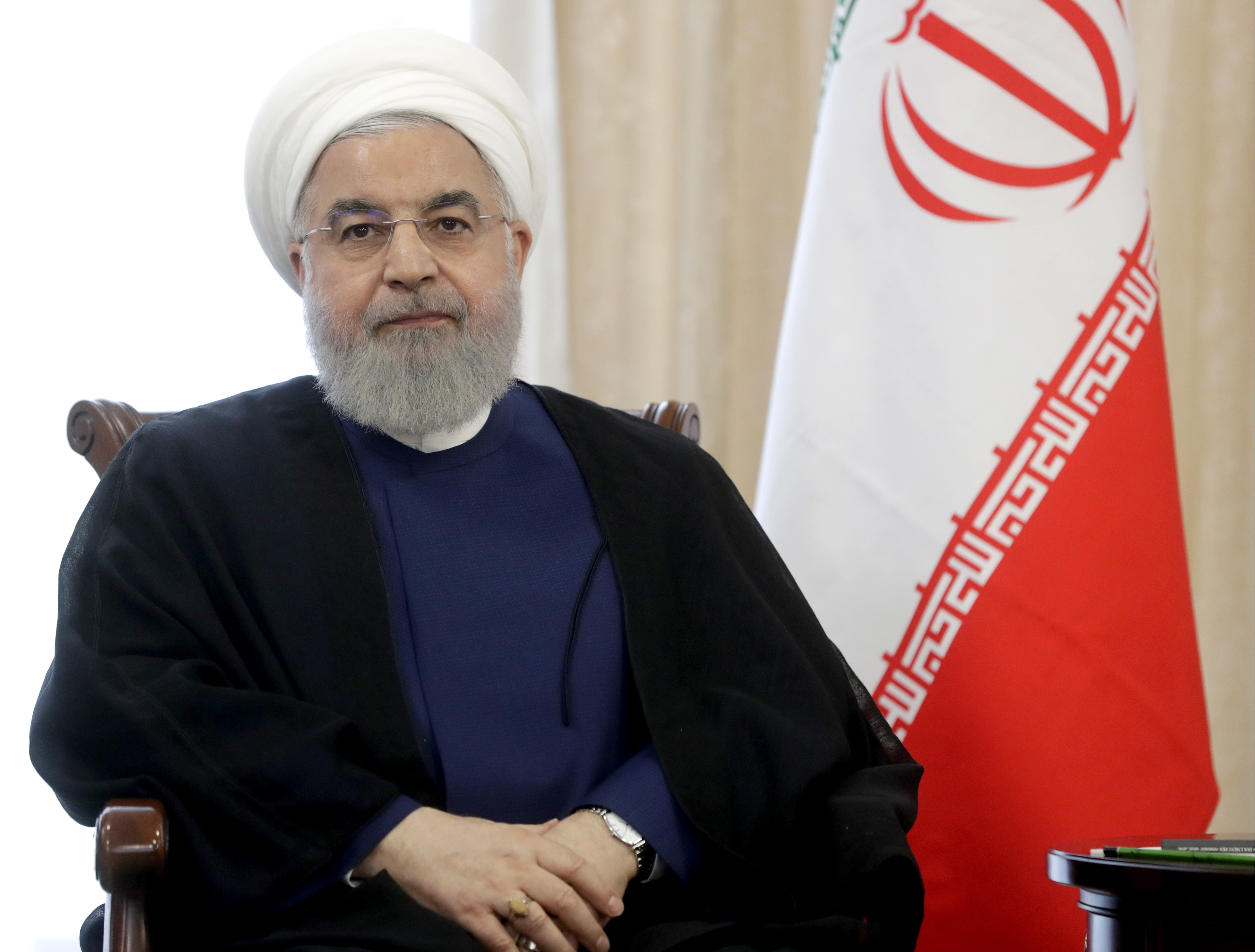 Iran’s President Hassan Rouhani sitting beside an Iranian flag.