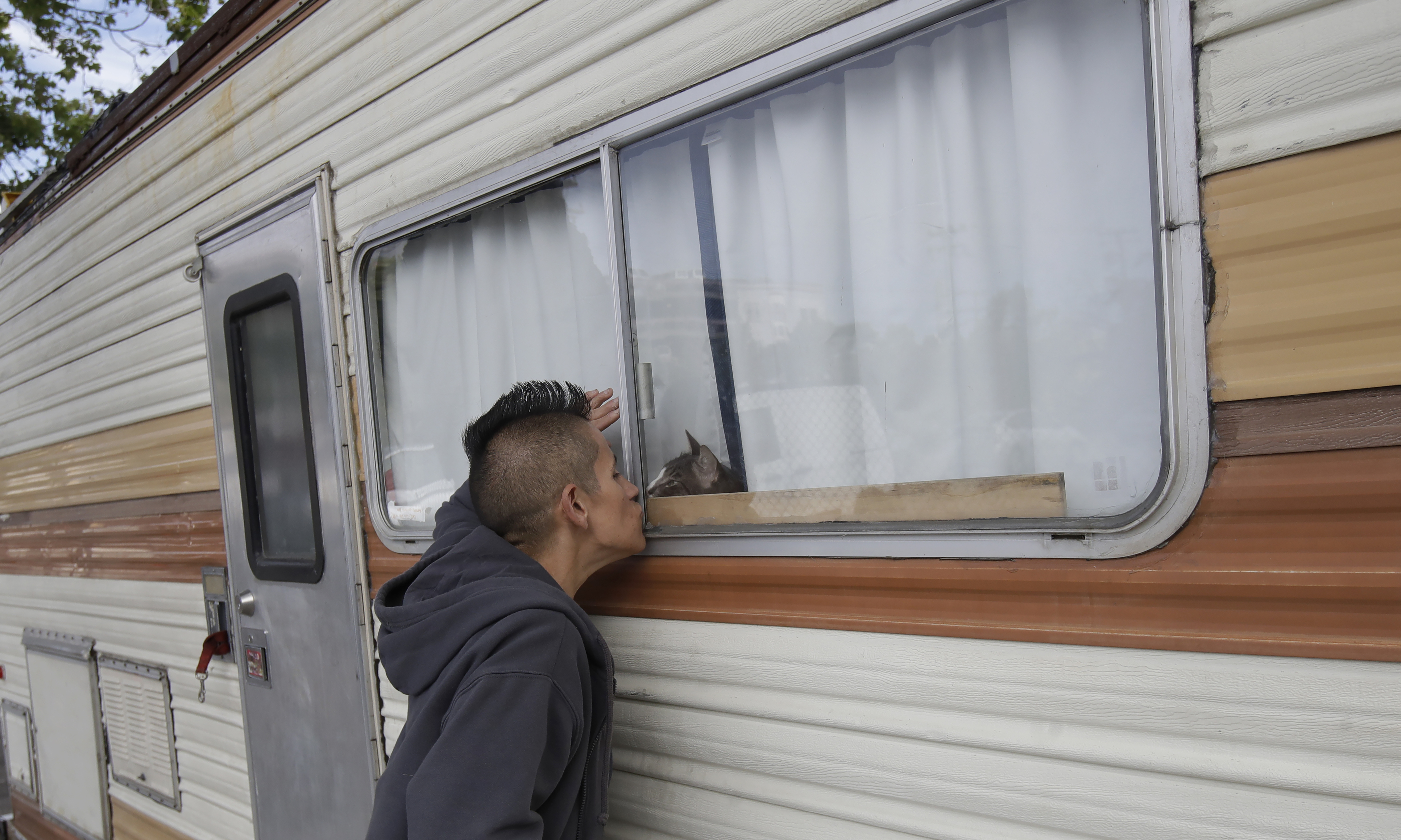 Shanna Couper Orona kisses her cat Maison through a window of her RV parked along a street in San Francisco.