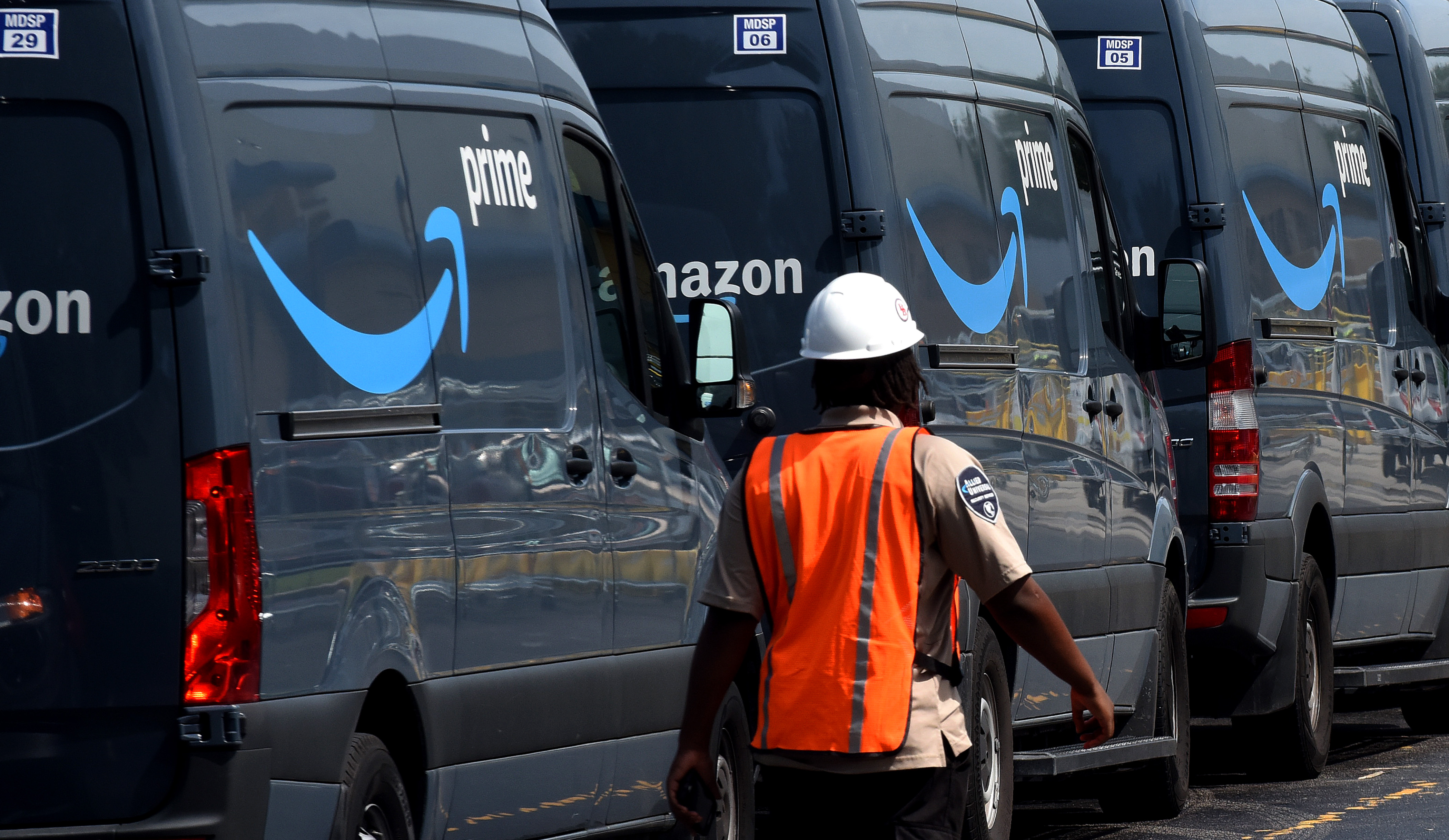 A worker walking past a line of Amazon Prime delivery vans.