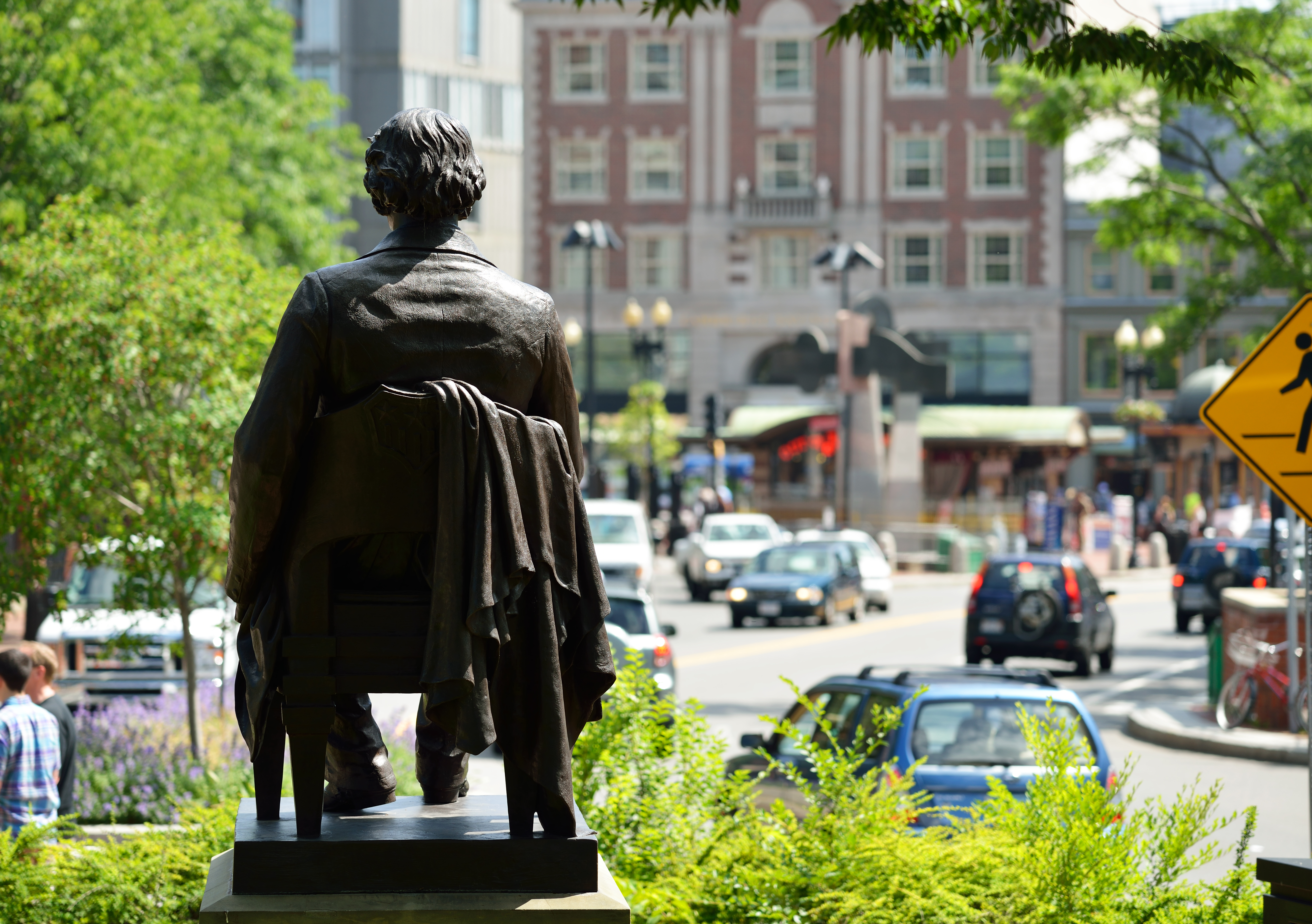A statue of a man seated overlooking a busy square in a city.