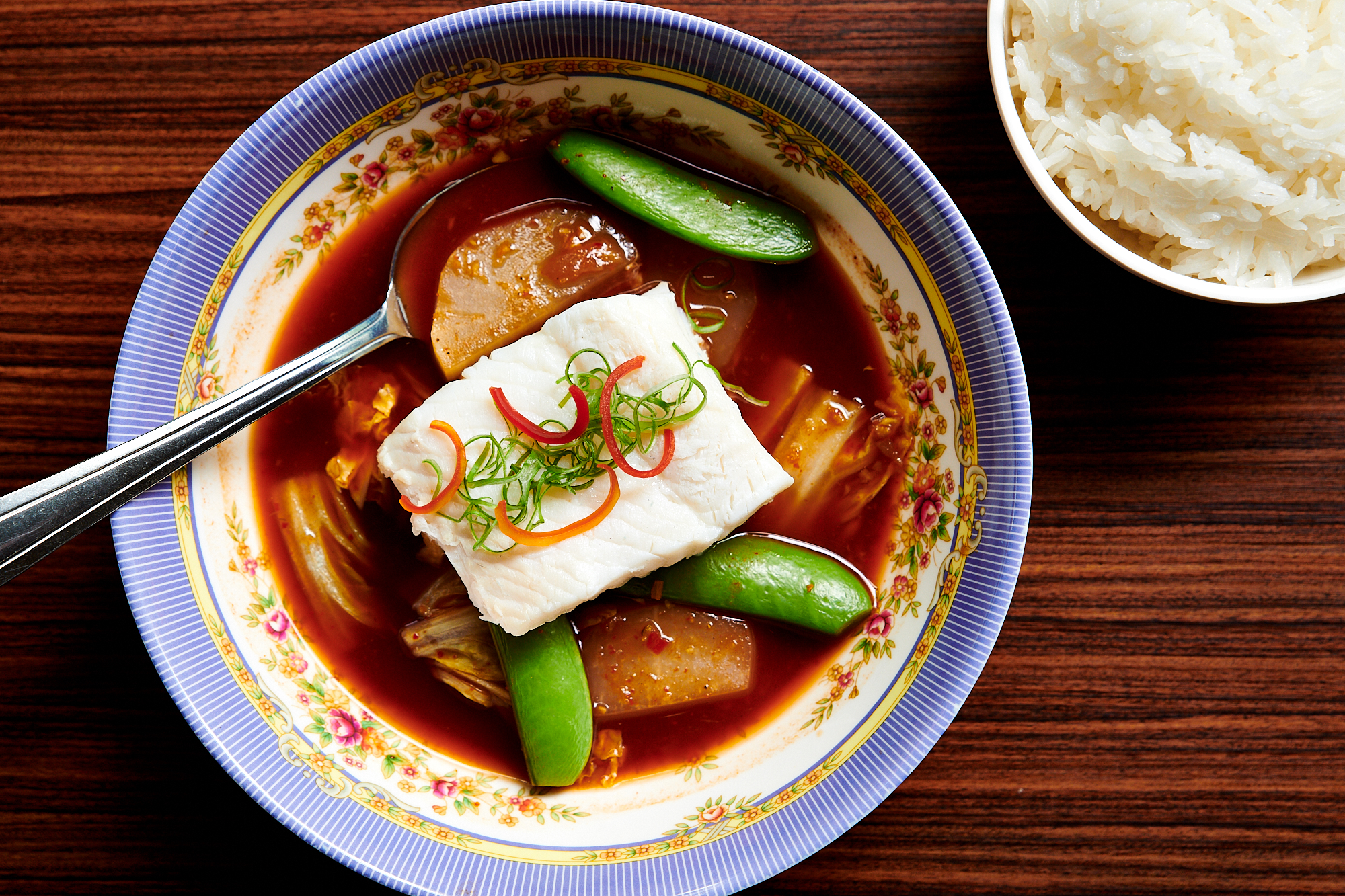 A picture of a red bowl of coconut-milk-free curry with a single chunk of halibut, pieces of cabbage, and snap peas. The curry is served in an ornate bowl with a side of rice.