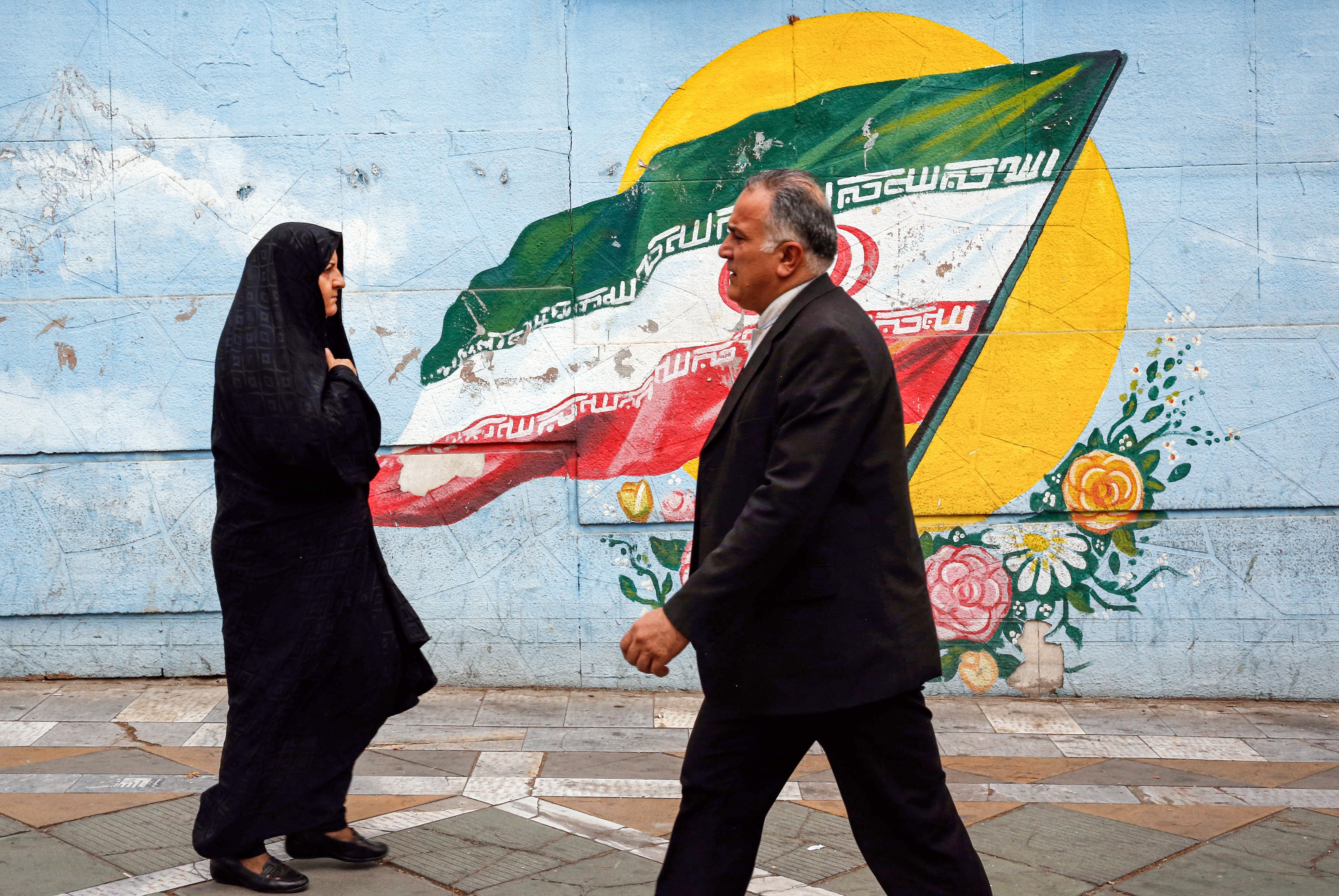 A man and a woman walk past a mural of the Iranian flag in Tehran on July 22, 2019.