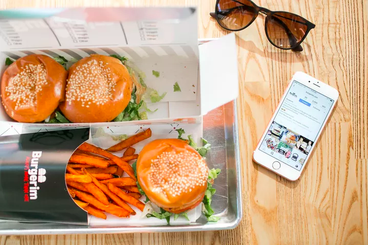three sliders with orange-colored fries on a table with sunglasses and a cellphone