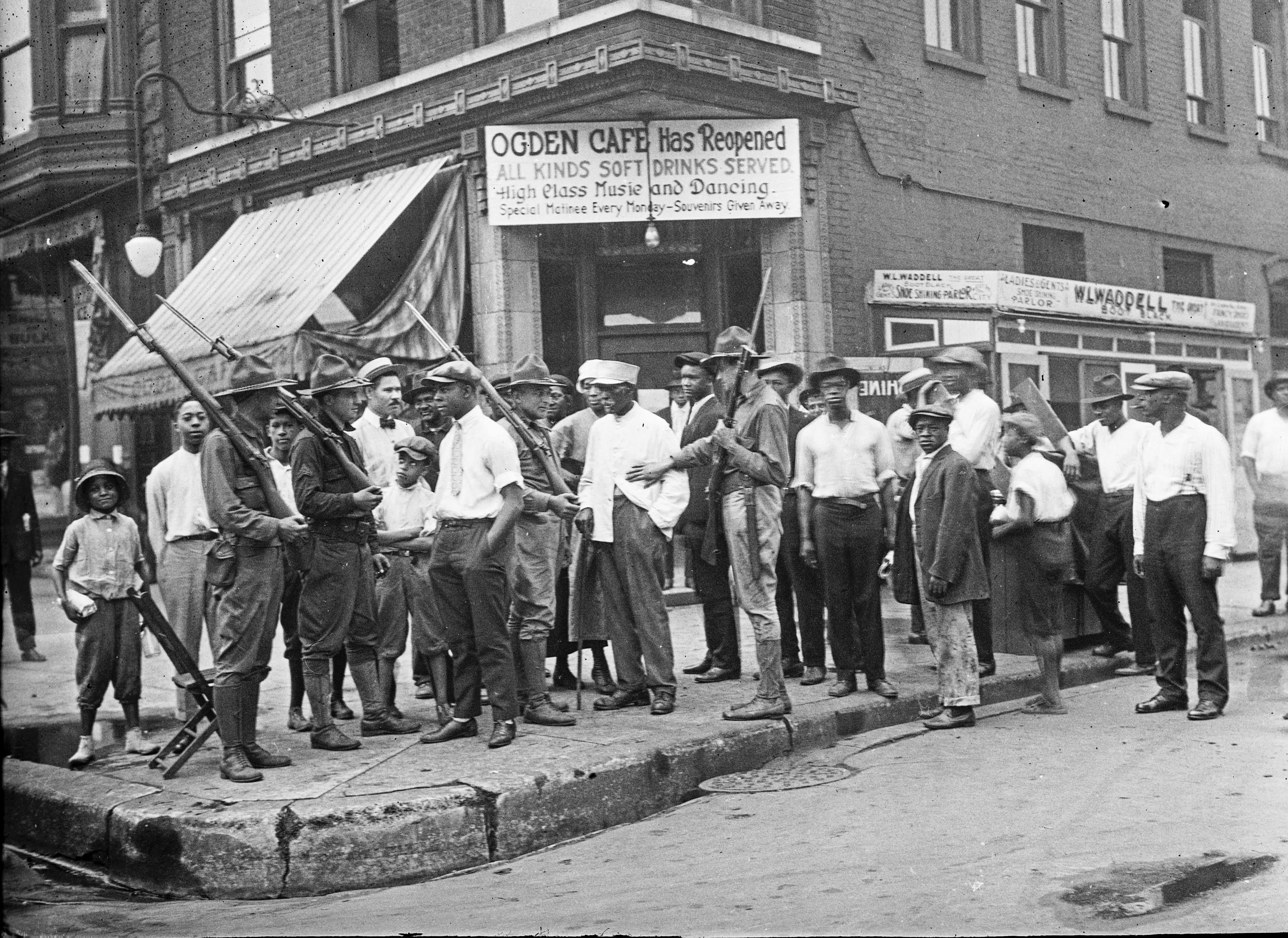A crowd of men and armed National Guard soldiers stand outside a cafe during the 1919 Race Riots in Chicago.