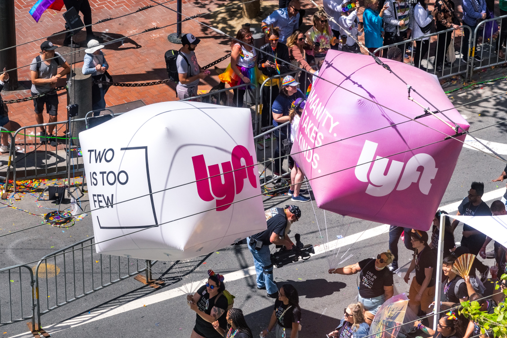 A pair of giant cubical balloons with the Lyft logo in a parade.