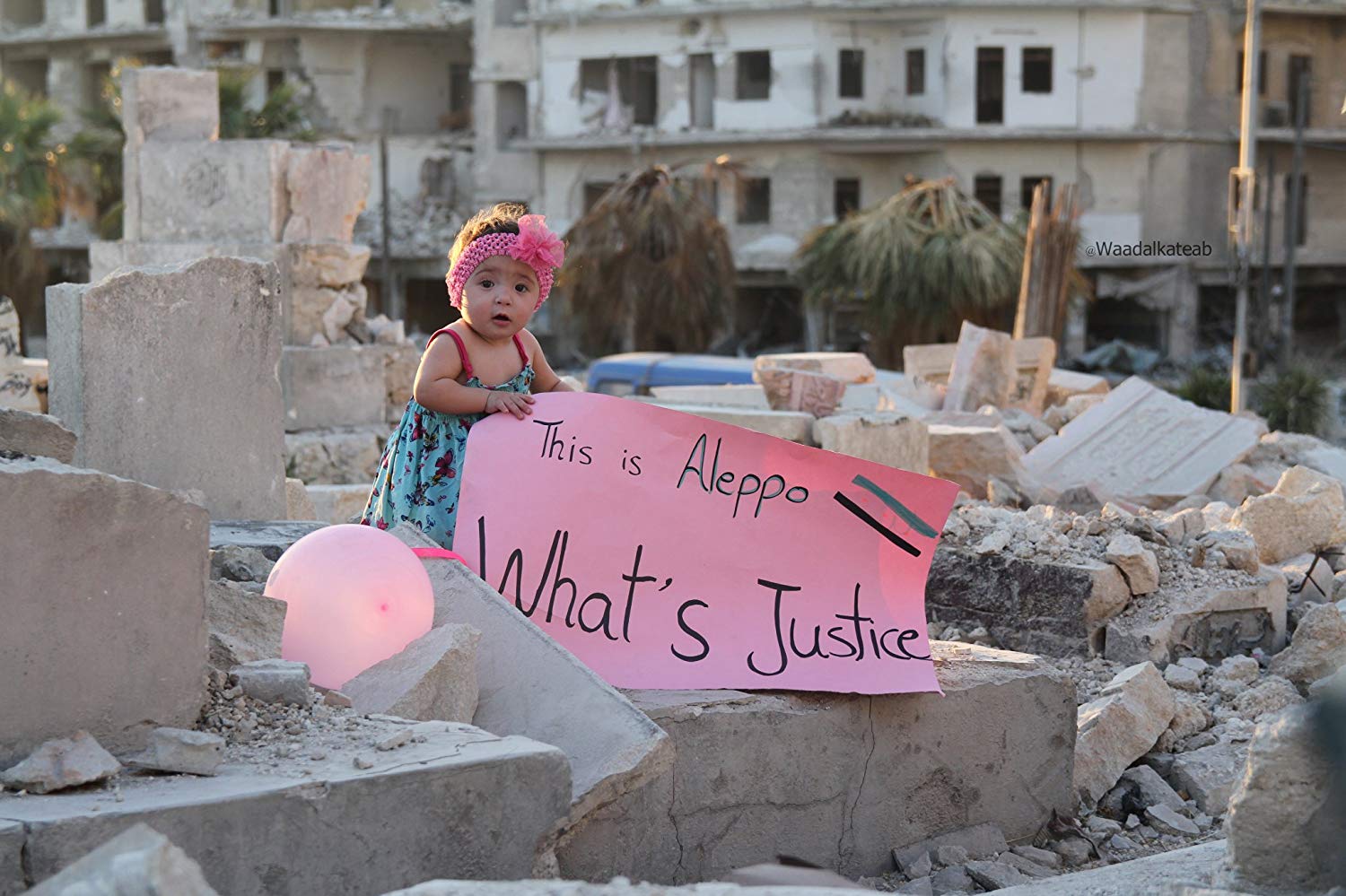 A scene from the documentary “For Sama” showing a toddler amid the wreckage of Aleppo holding a sign that reads, “What’s justice.”