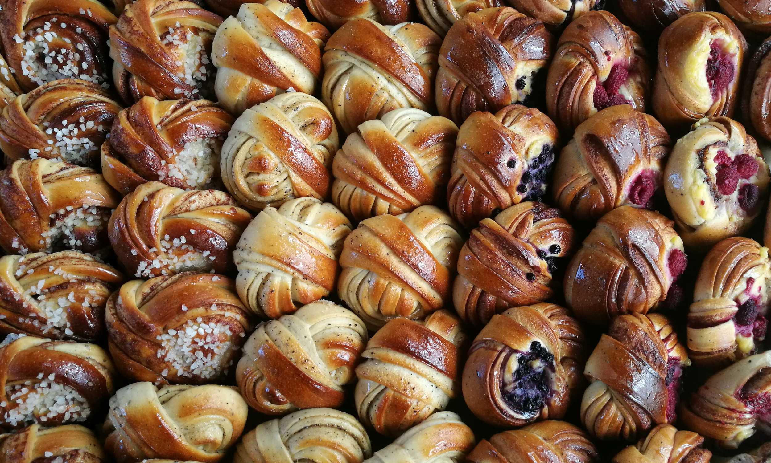 A tightly packed tray of knotted Scandinavian buns, with cardamom, cinnamon, vanilla, and raspberry