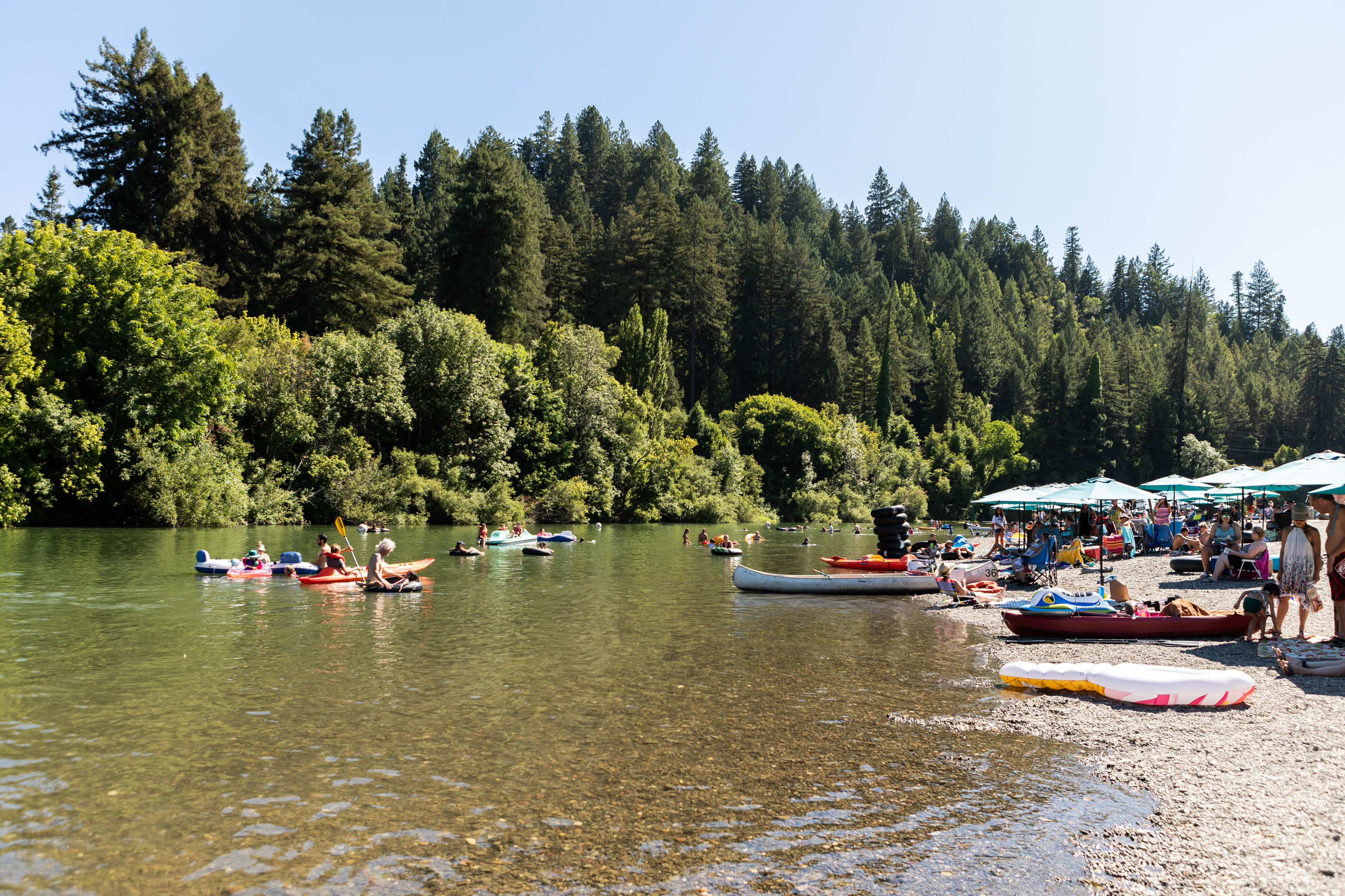Scene of the Russian River in Guerneville in the sunlight with boats and families on the water.