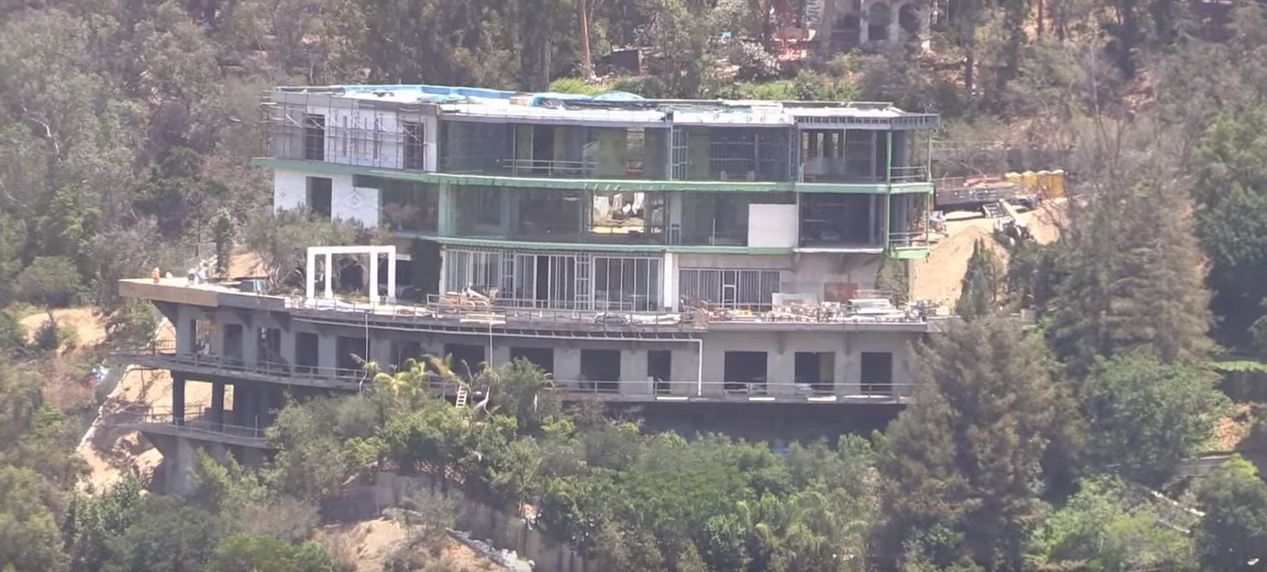 An aerial photo of a half-finished mansion jutting out of a hillside.