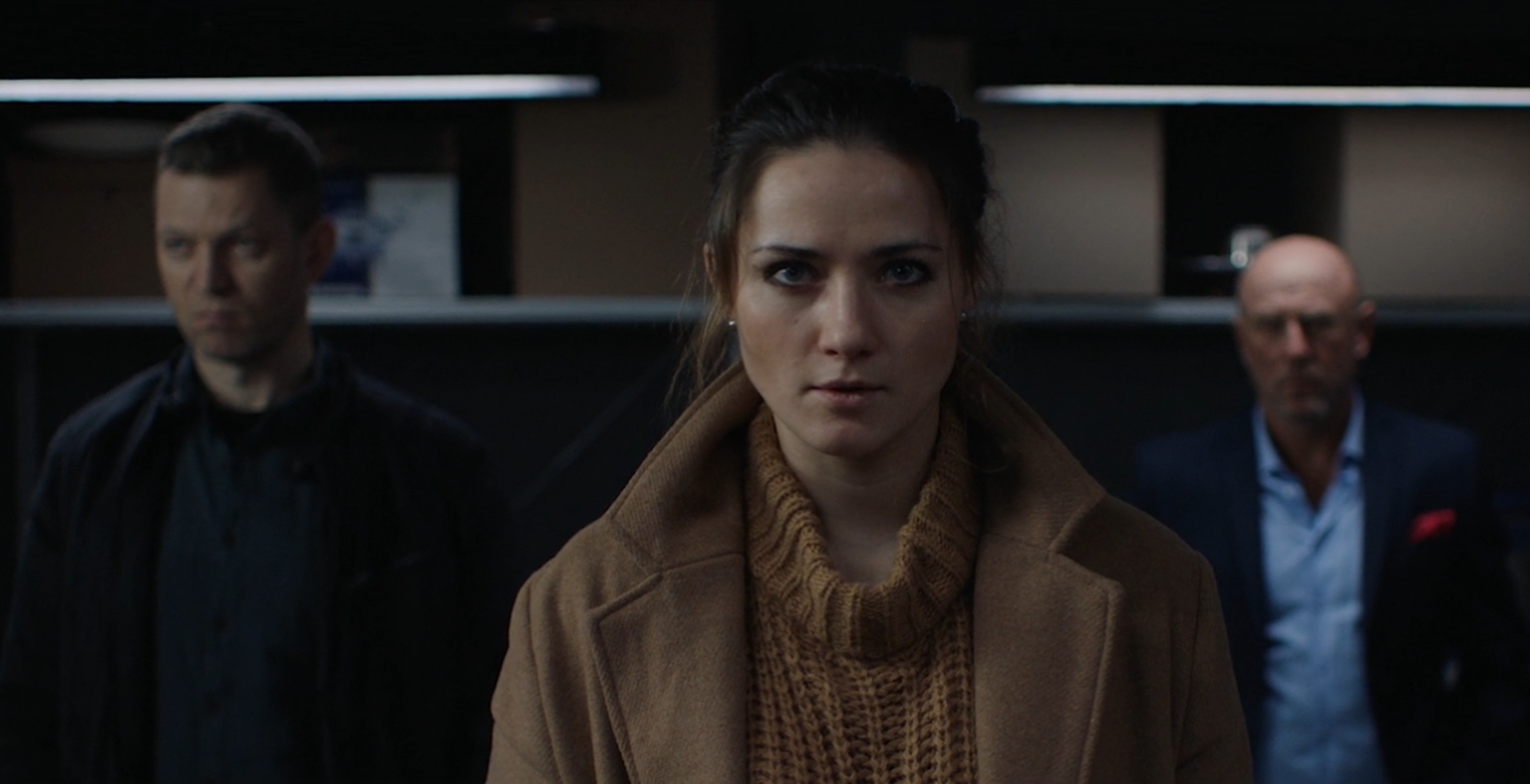 a serious-looking woman in a sweater is flanked by two angry-looking men in She Sees Red