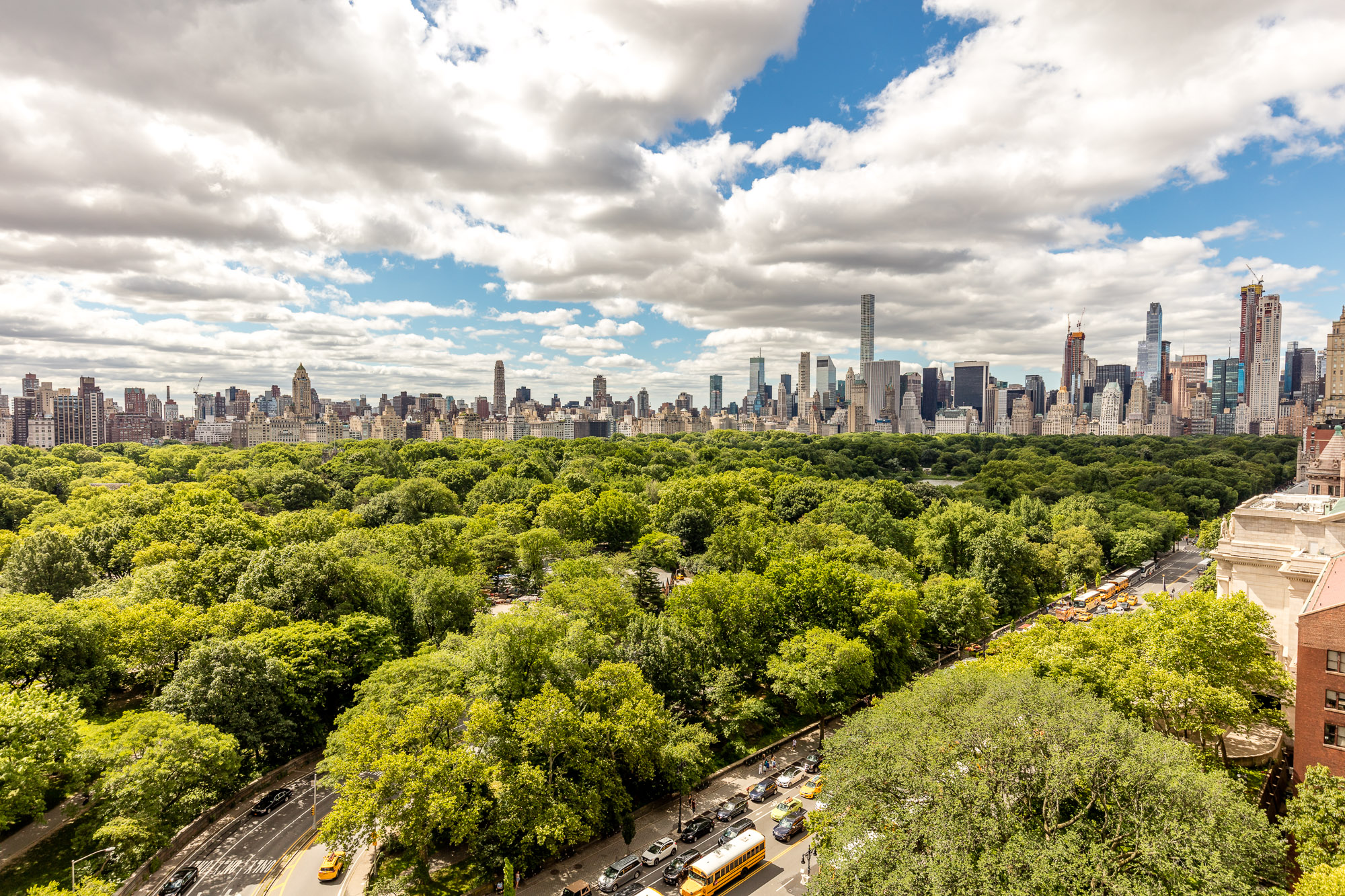 Aerial view of green trees in Central Park, with tall buildings in Manhattan in the background, and a blue sky. 