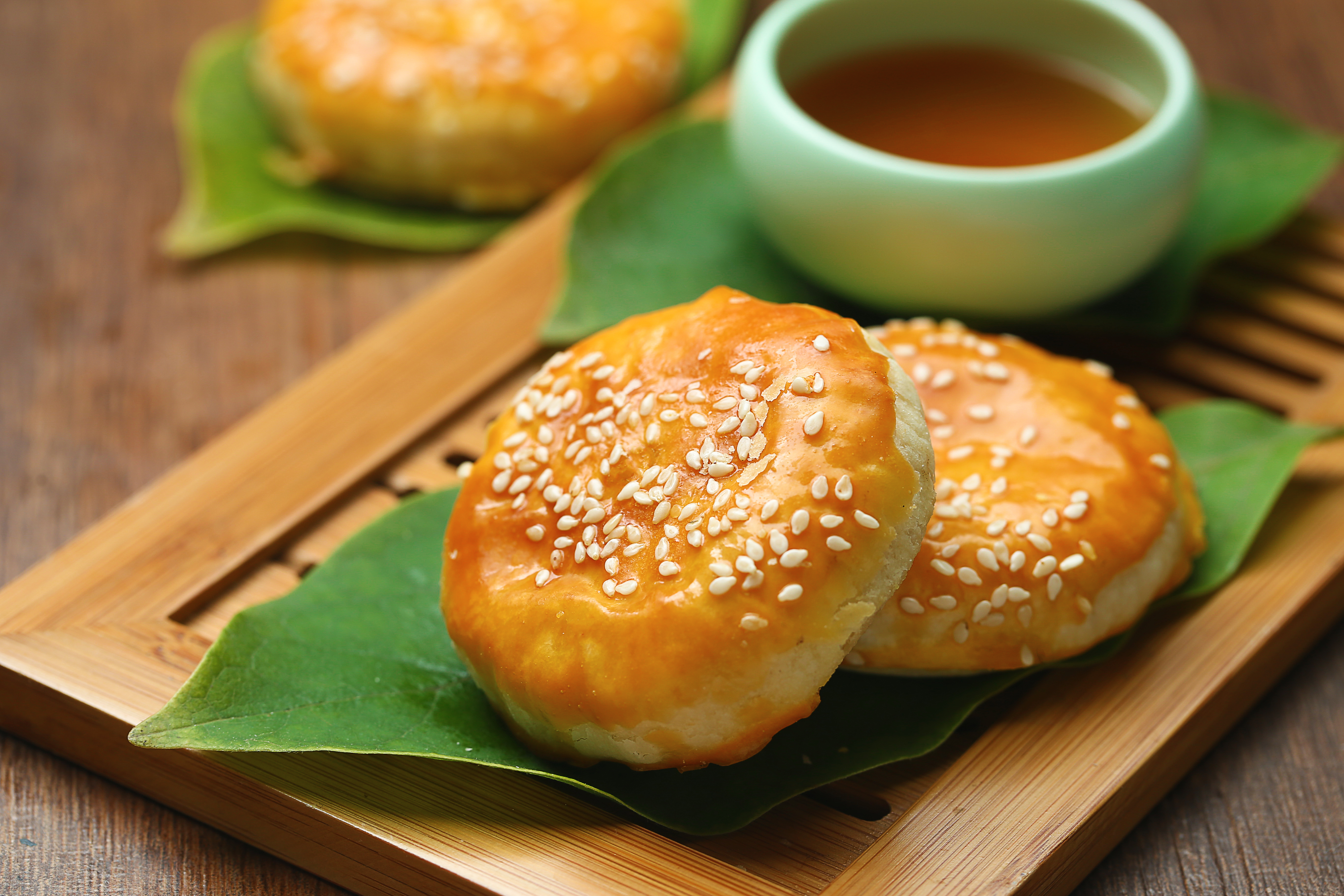 Wife cakes, or sweetheart cakes, sprinkled with sesame are presented on a palm leaf with tea.