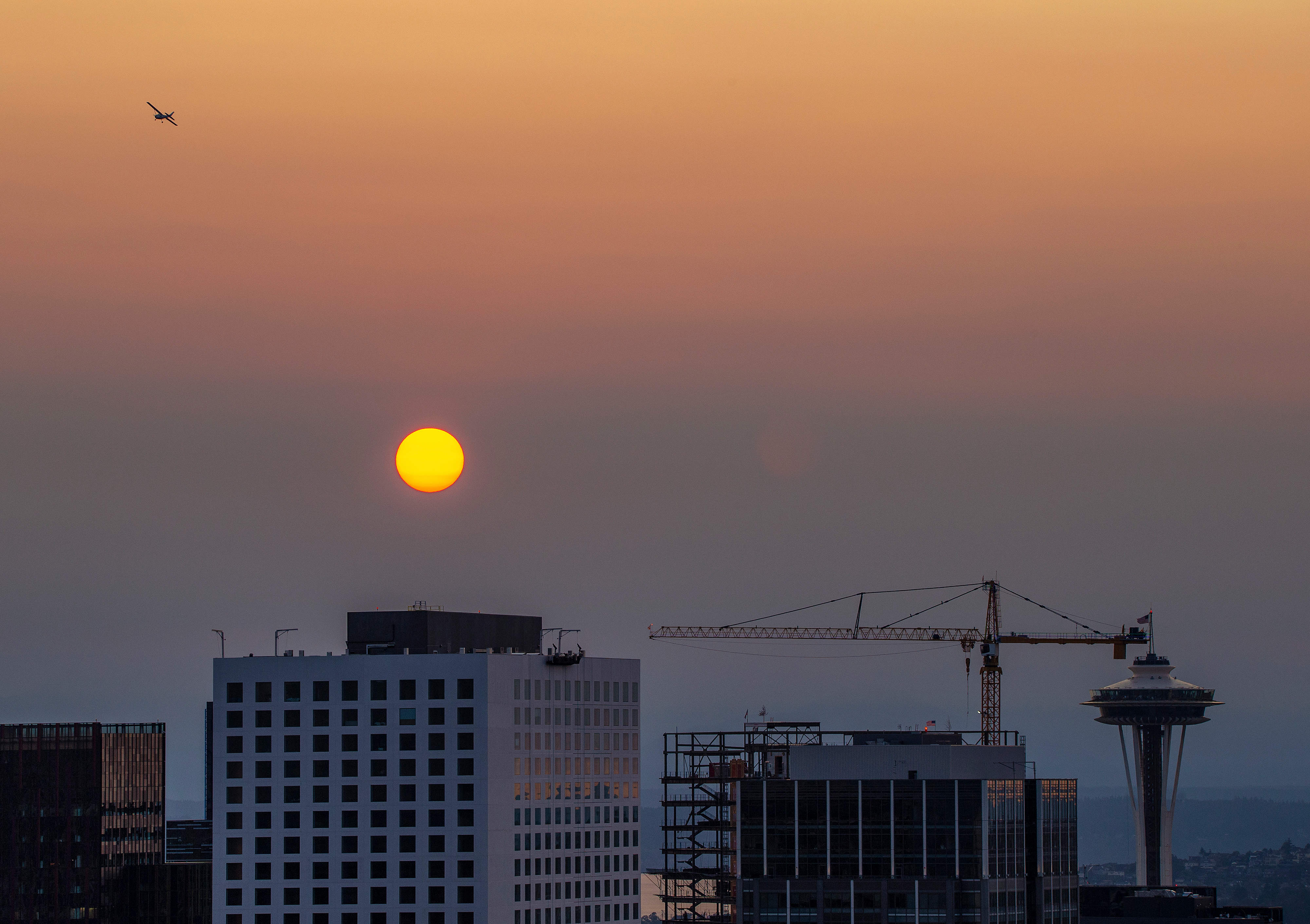 The Space Needle, a construction crane, and some buildings underneath a smoky backdrop, with a red sun.