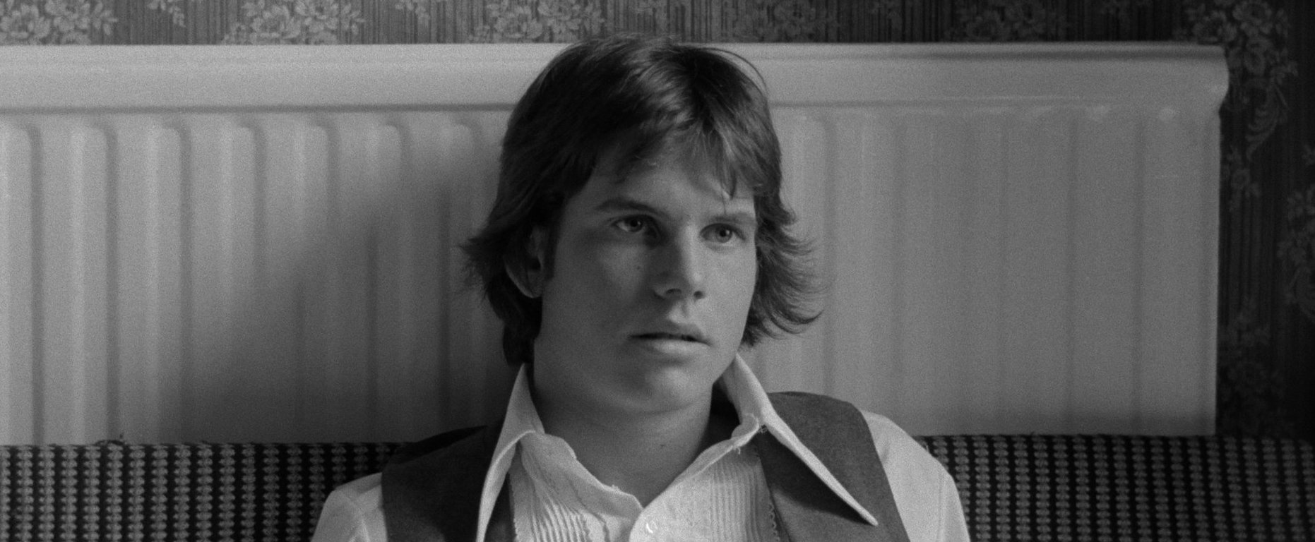 Bill Paxton sitting against a wall, mouth agape in the black-and-white film Taking Tiger Mountain