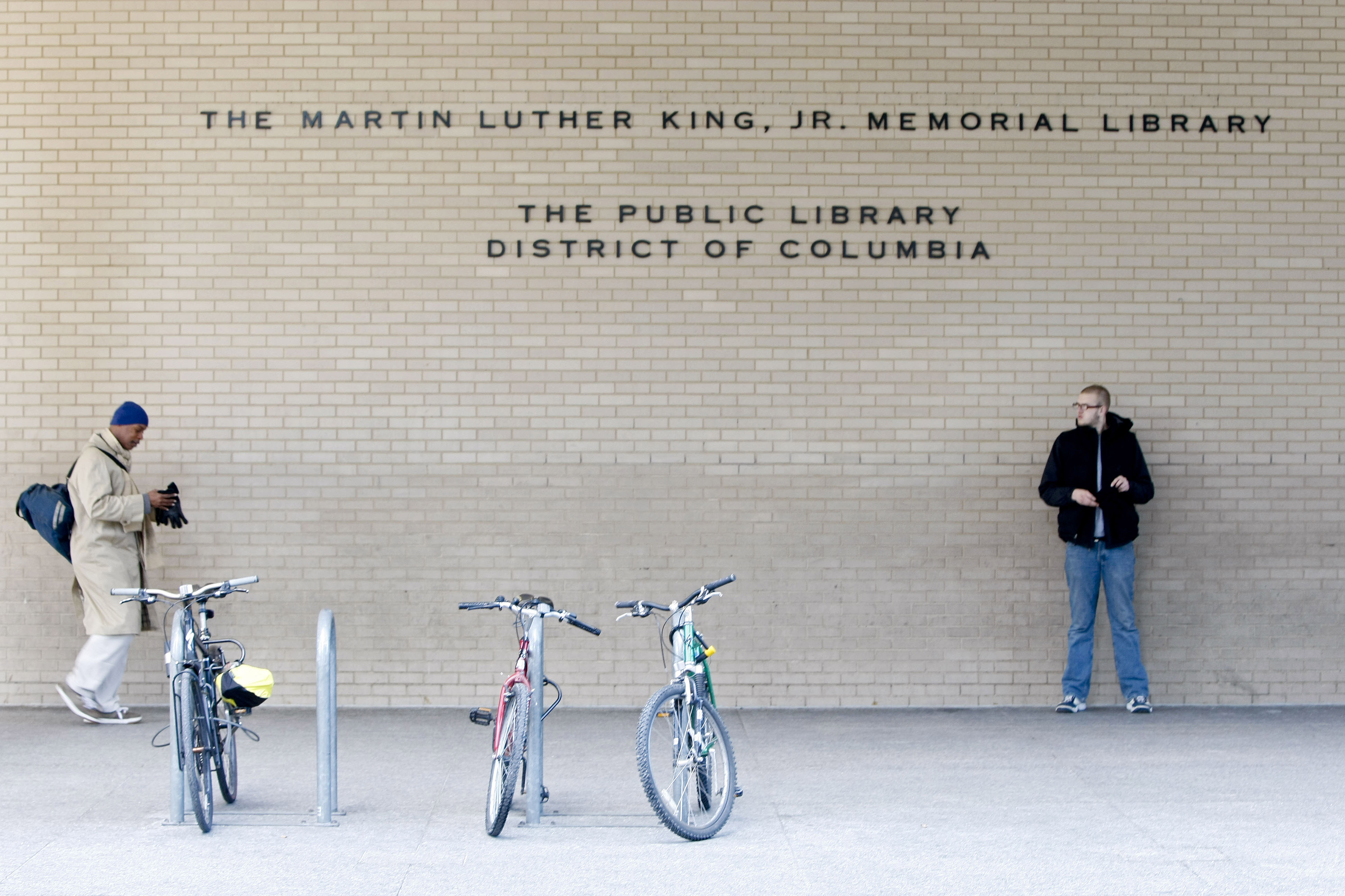 The brick facade of the Martin Luther King Jr. Library up close, with two men standing out front.