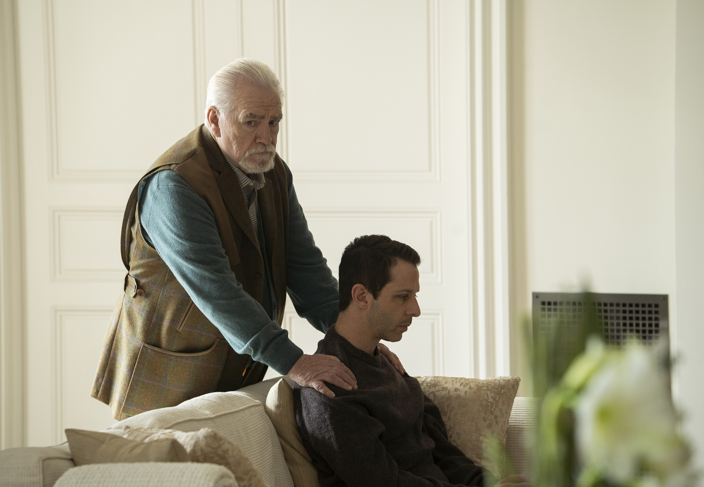 a melancholy scene on Succession: Kendall sits on a couch while his father, Logan, comforts him by putting his hands on Kendall’s shoulders