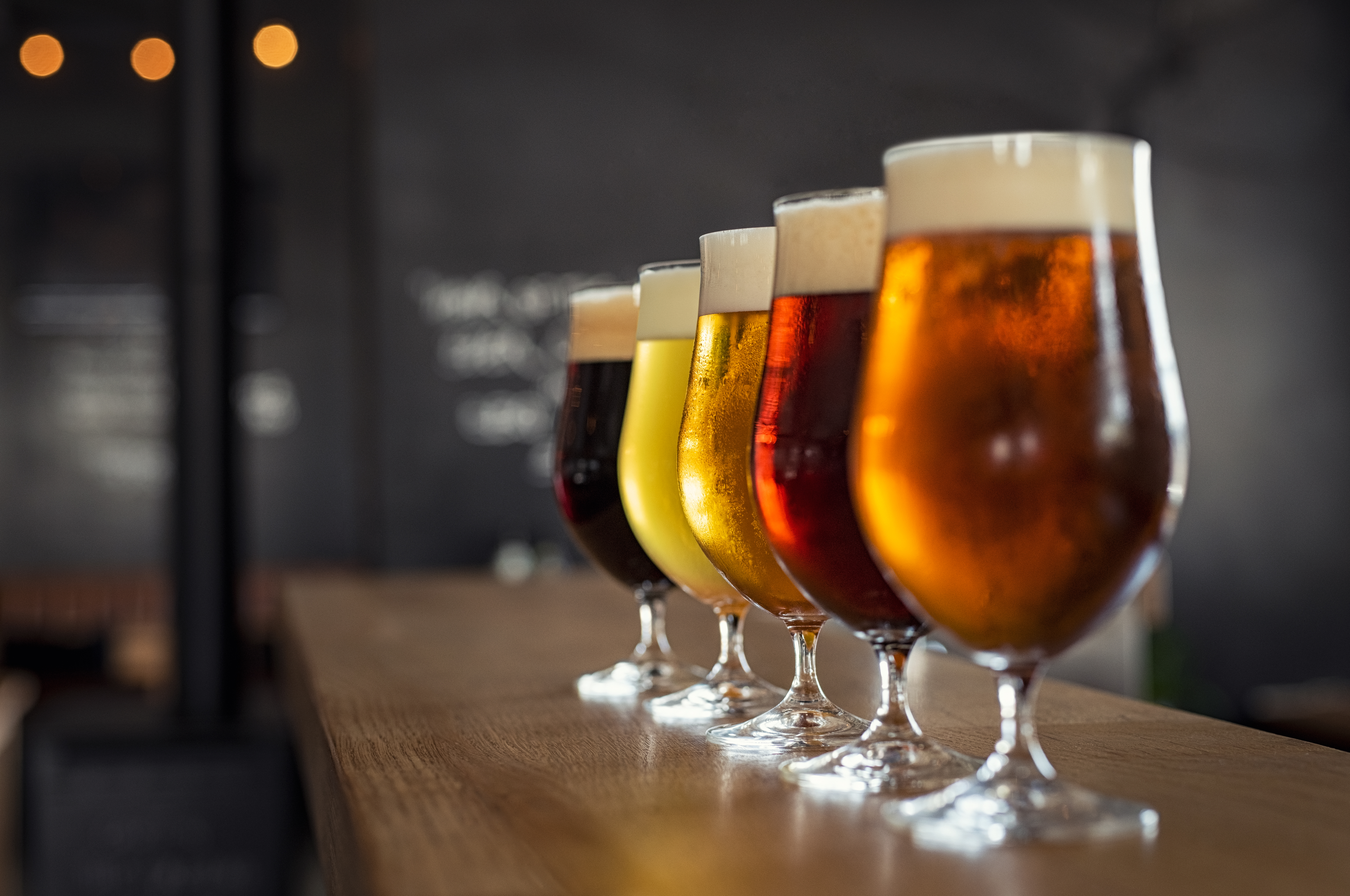Stock photo of beer —&nbsp;five glasses, each with a beer of a different color, are lined up on a bar
