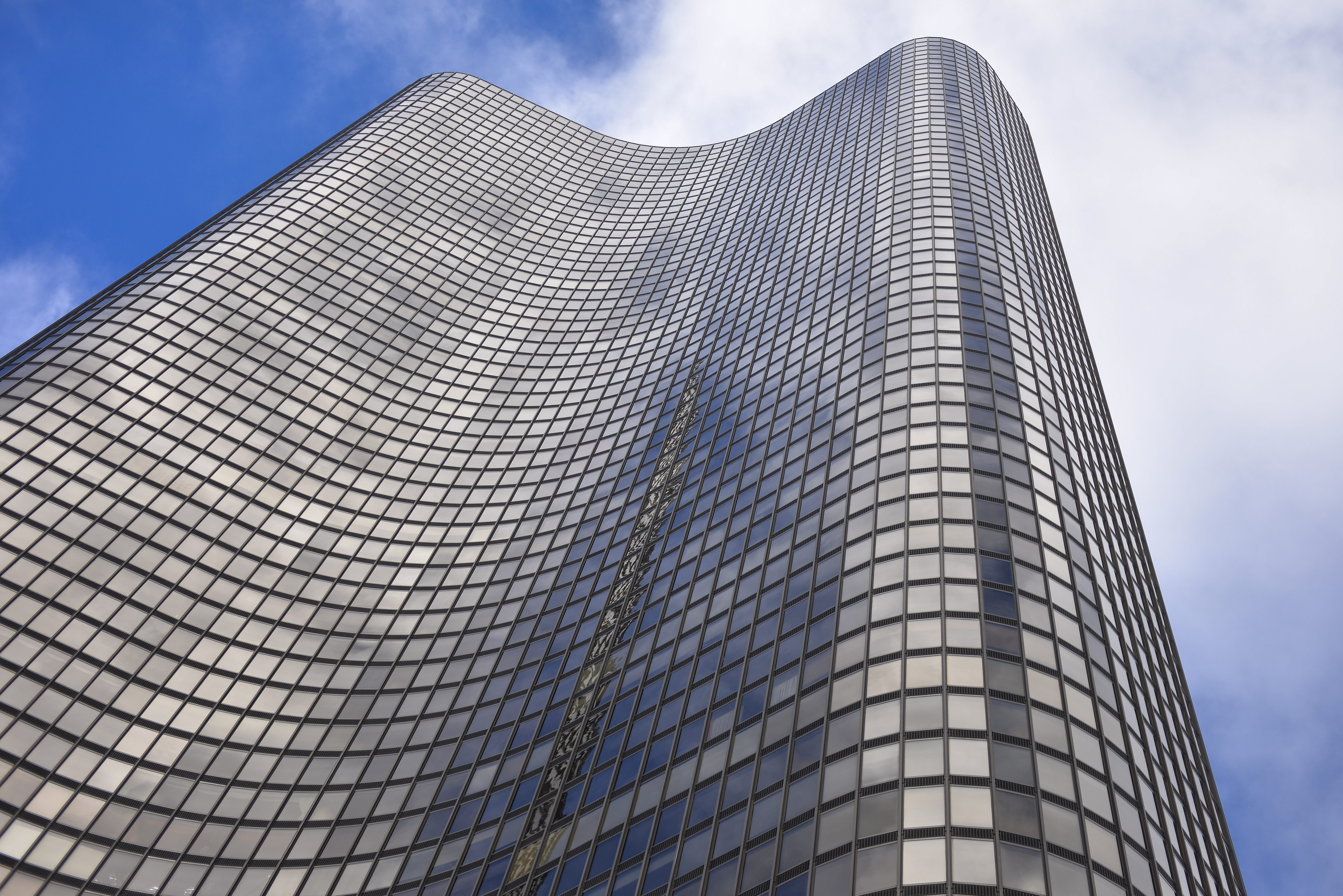 Looking up a a black, 70-story building with three curving lobes clad in a dark glass and aluminum facade.