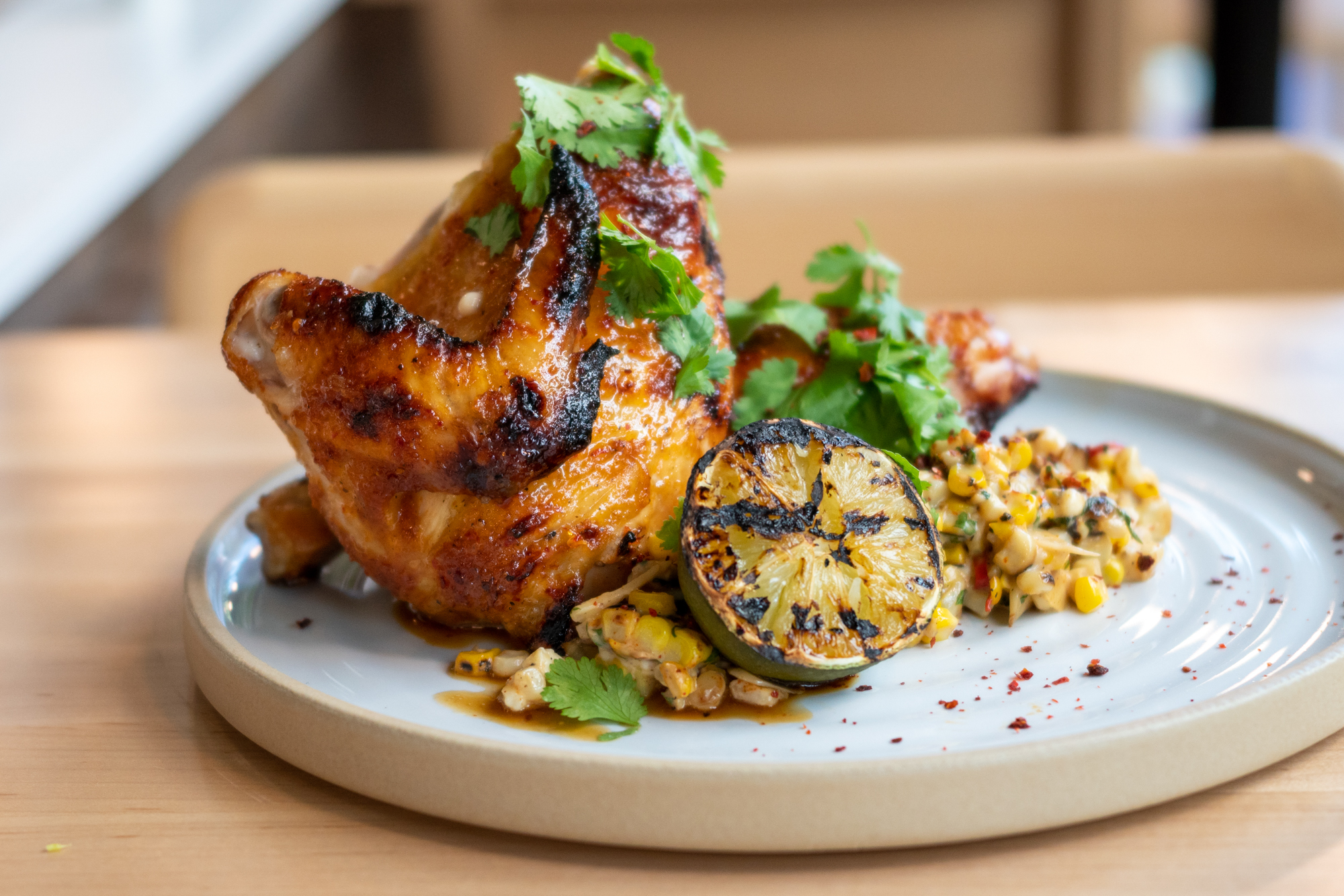 A plate of half smoked chicken with grilled lime and corn, drizzled with green herbs.