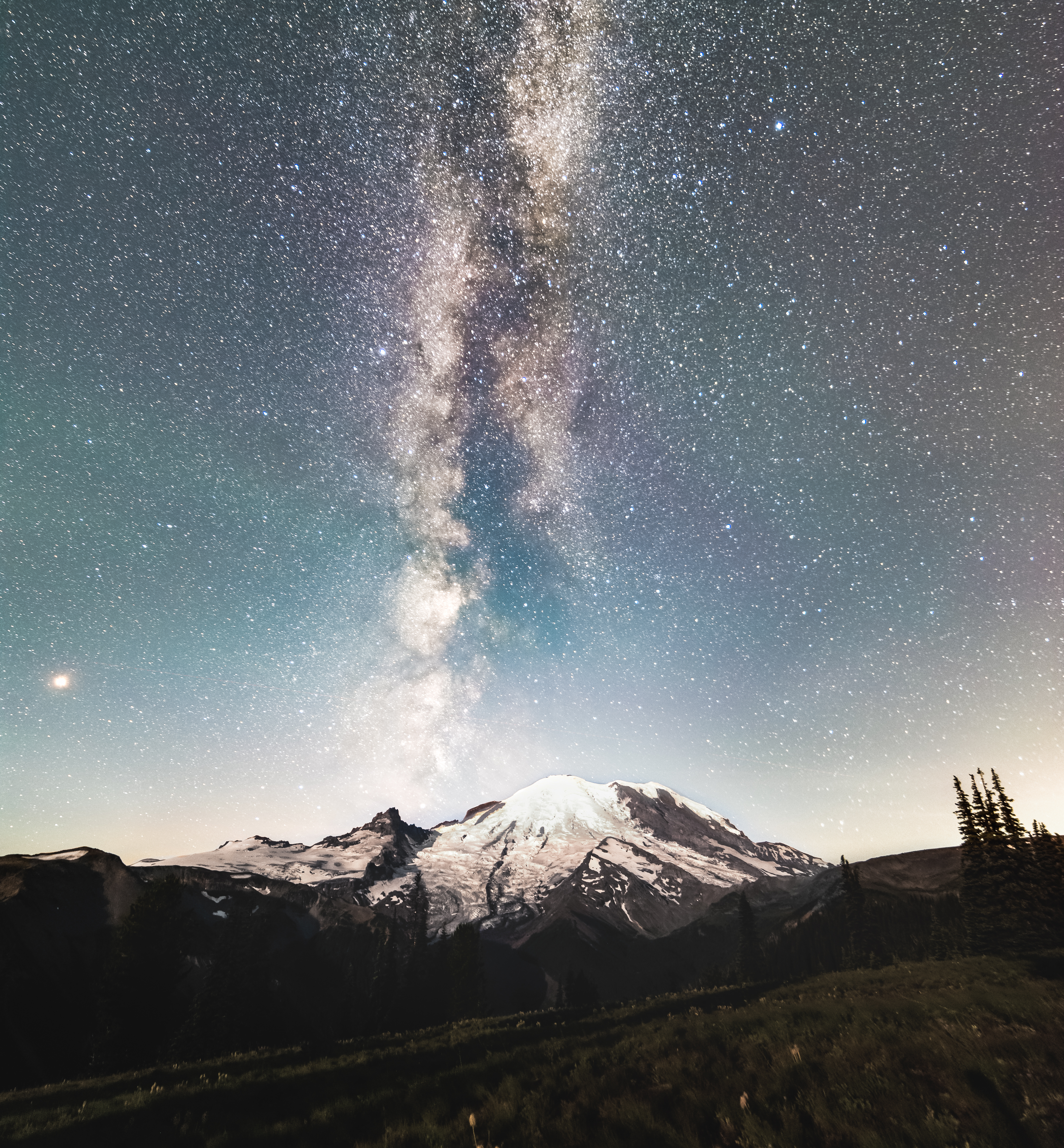 Stars are visible in the night sky over a mountain, with a dense, milky stretch of stars (the Milky Way) up the center.