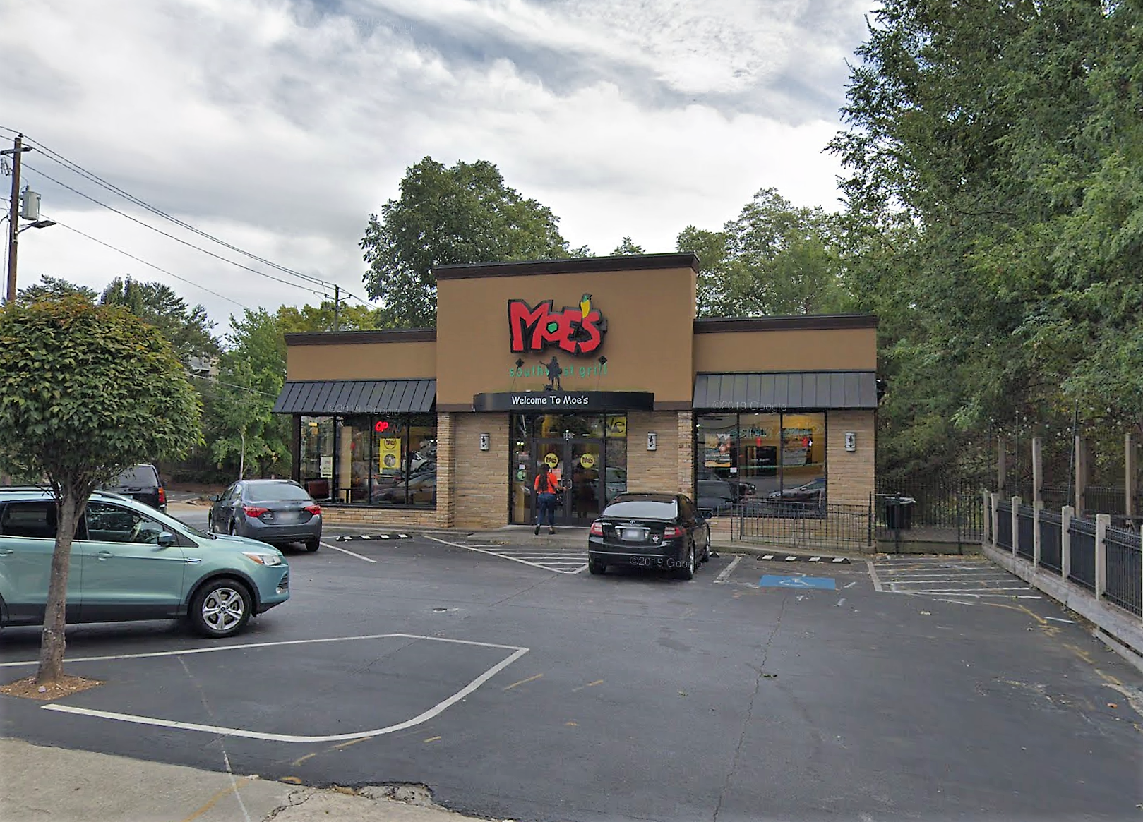 A tan, stucco-faced restaurant with the bright red Moe’s logo in front of the trees of Freedom Park.