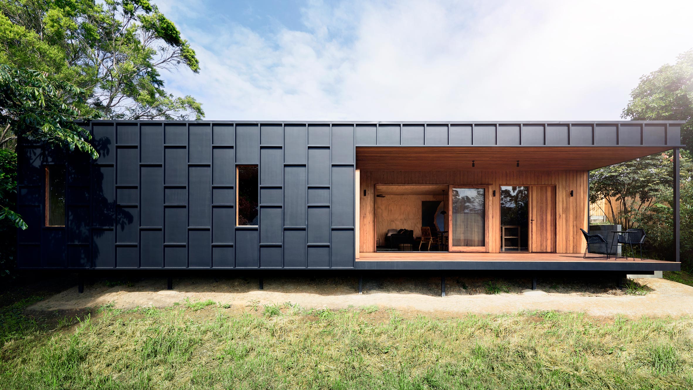 A single-story house featuring dark panel cladding and a cut-out opening to the interior, which is lined in plywood. 