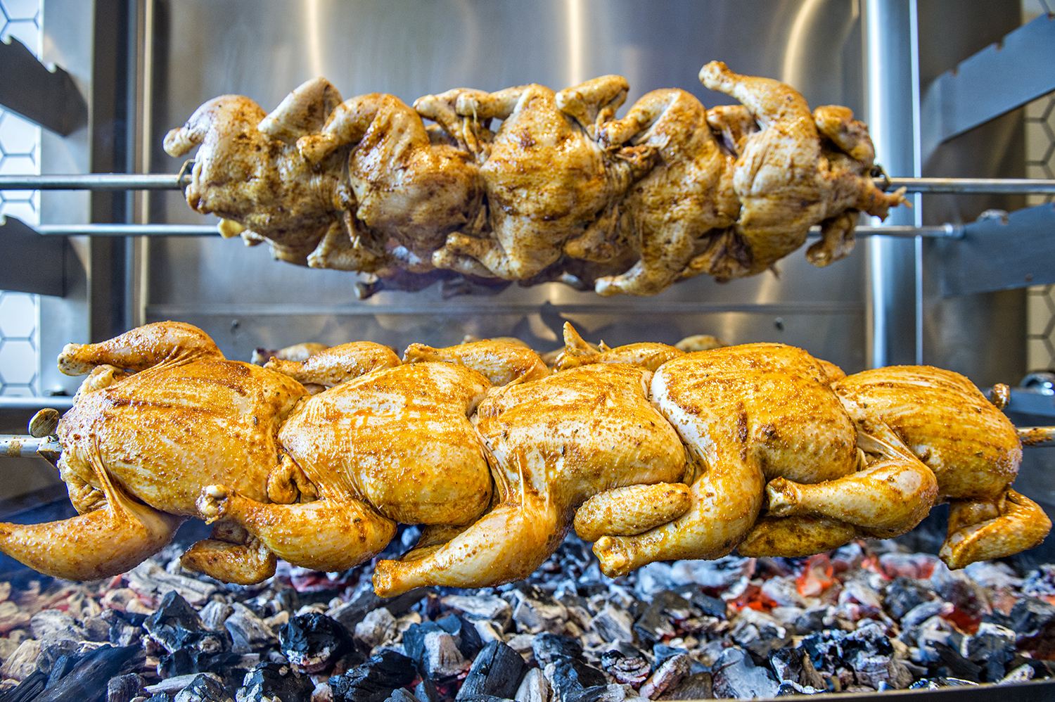 A close-up photo of two line of rotisserie chickens cooking on skewers
