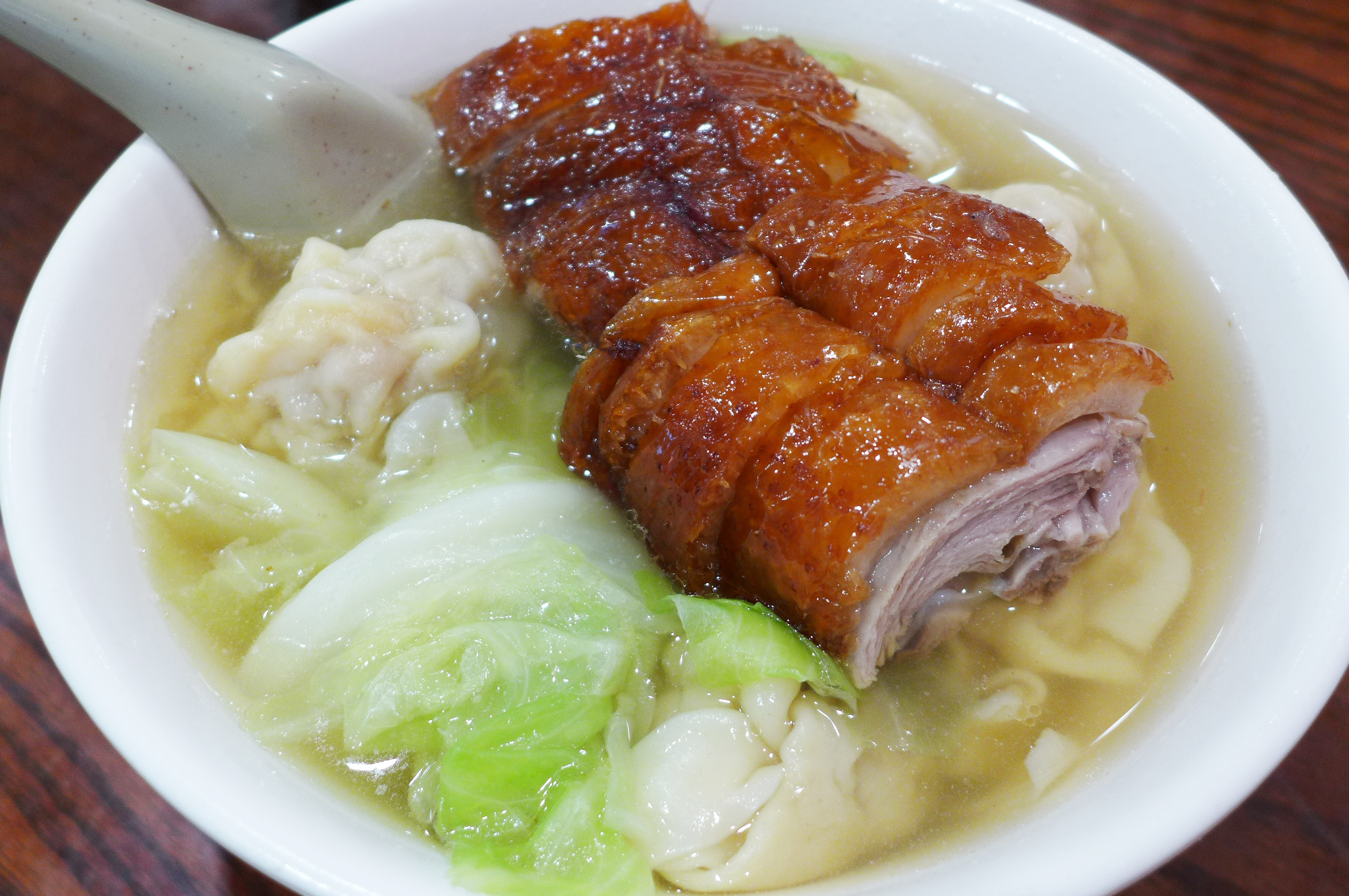 Chicken soup with roast duck, wontons, noodles, and cabbage in a white bowl
