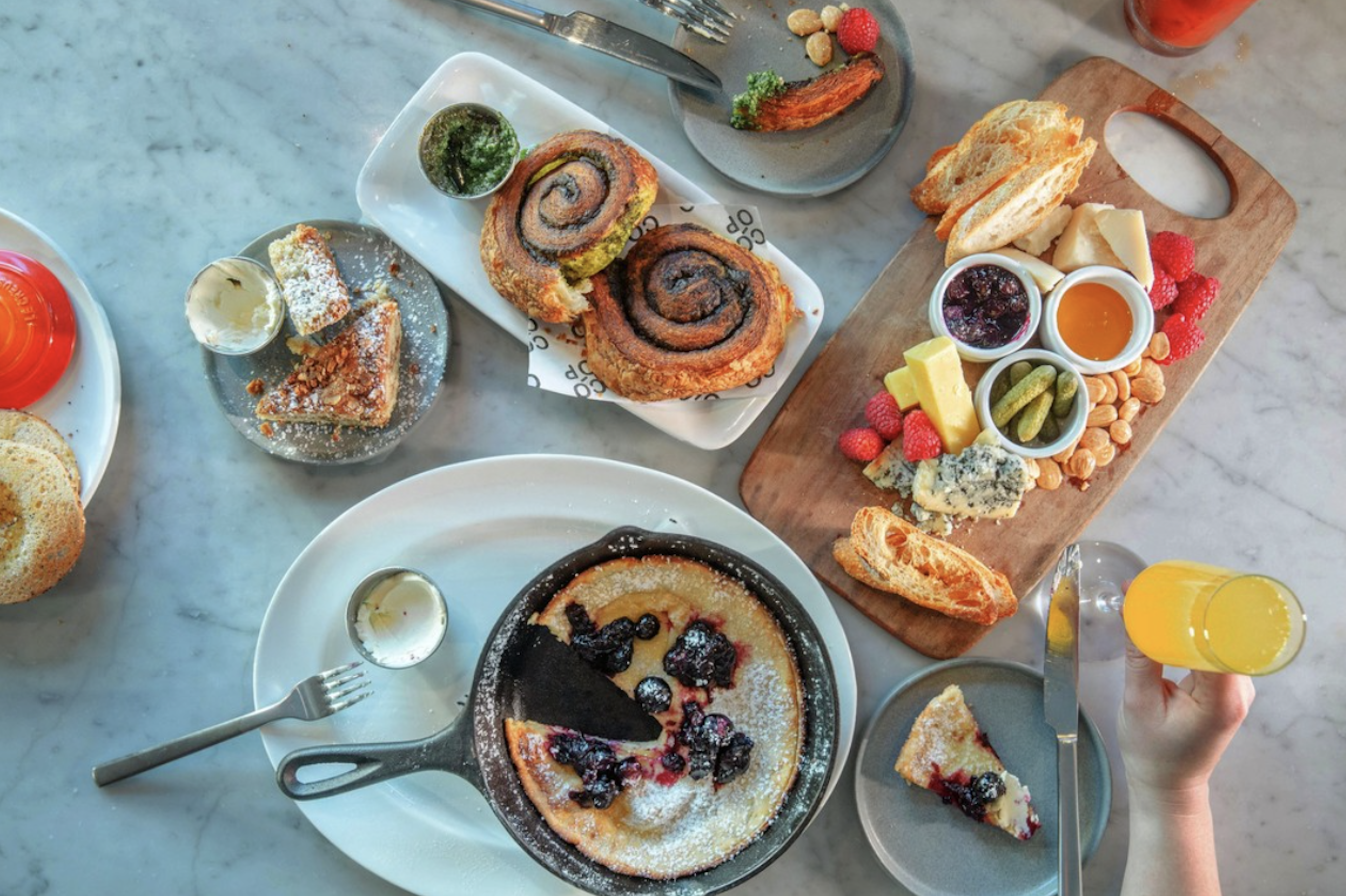 A dining table with popular brunch dishes next to each other such as morning buns, skillet coffee cake, and a dutch baby with blueberries.&nbsp;