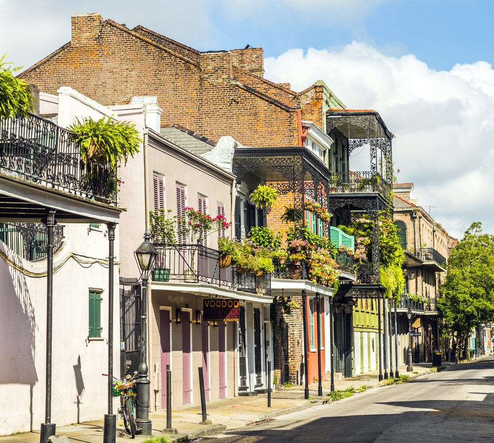 A row of two-story brick townhomes with plant-hung balconies in the French Quarter of New Orleans