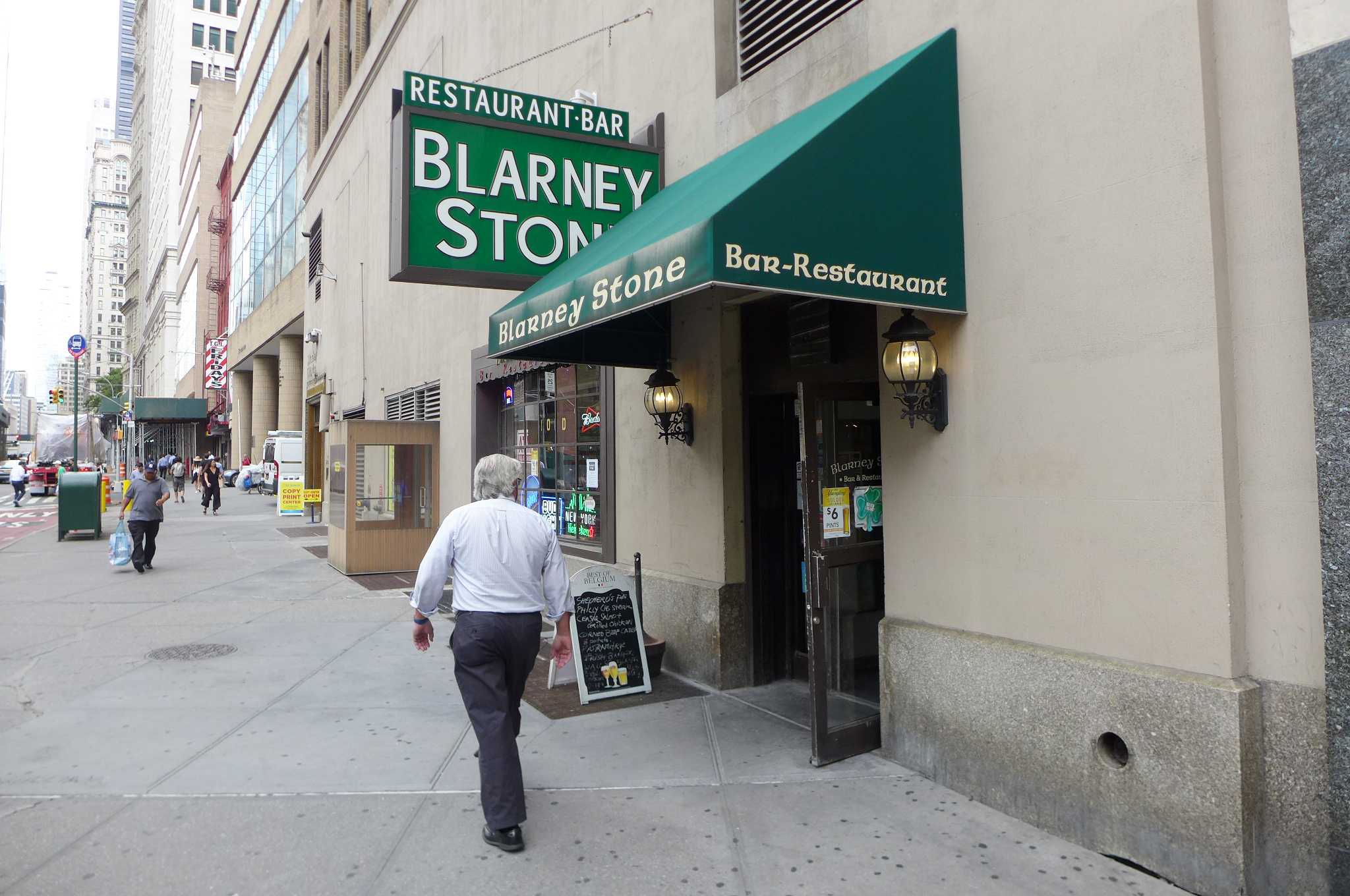 A green awning and green sign that says Blarney Stone, with a man walking away...